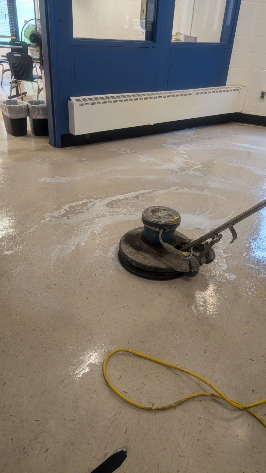 Floor buffer machine on a wet warehouse floor near a blue industrial wall and yellow cord.