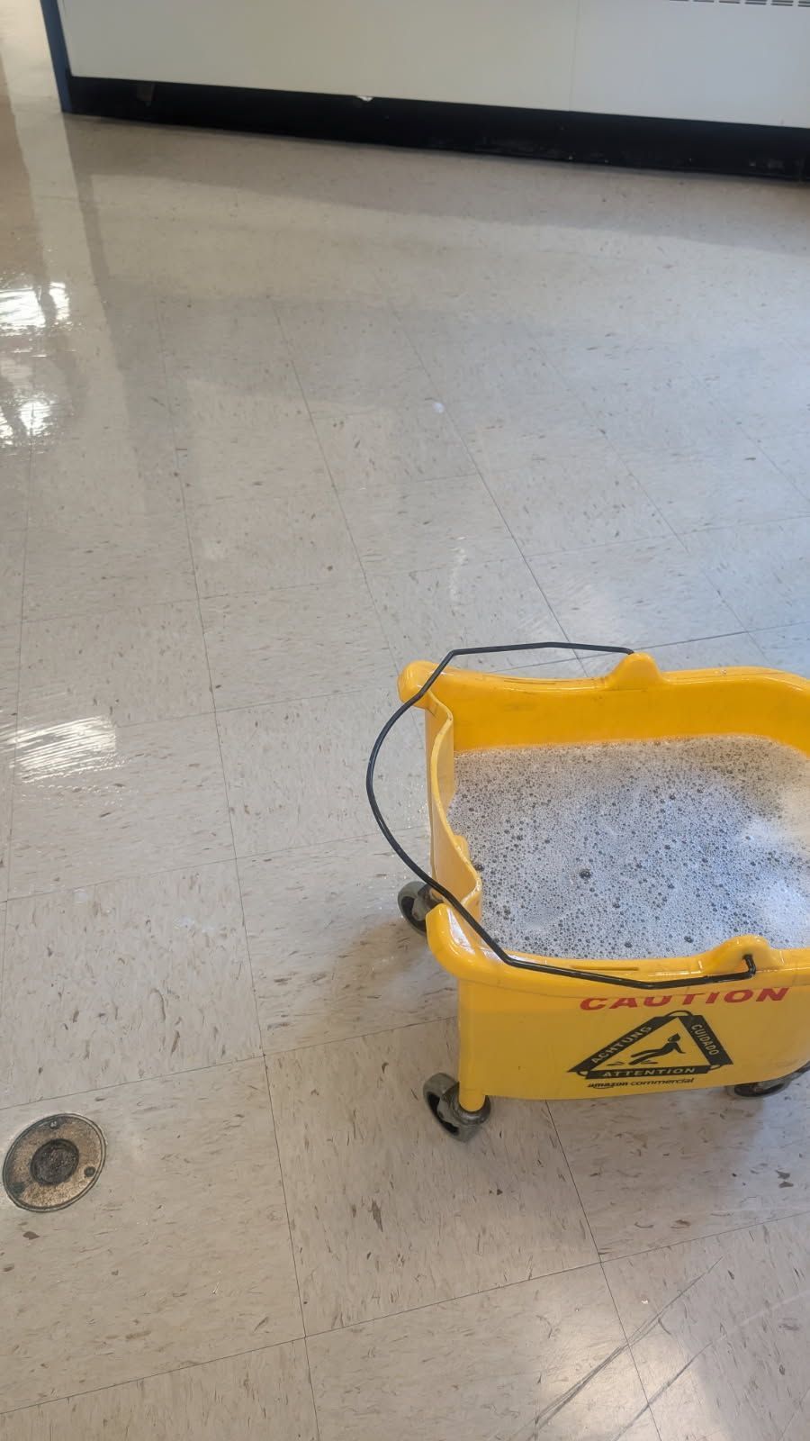 Yellow caution sign on a shiny tiled floor in a hallway.