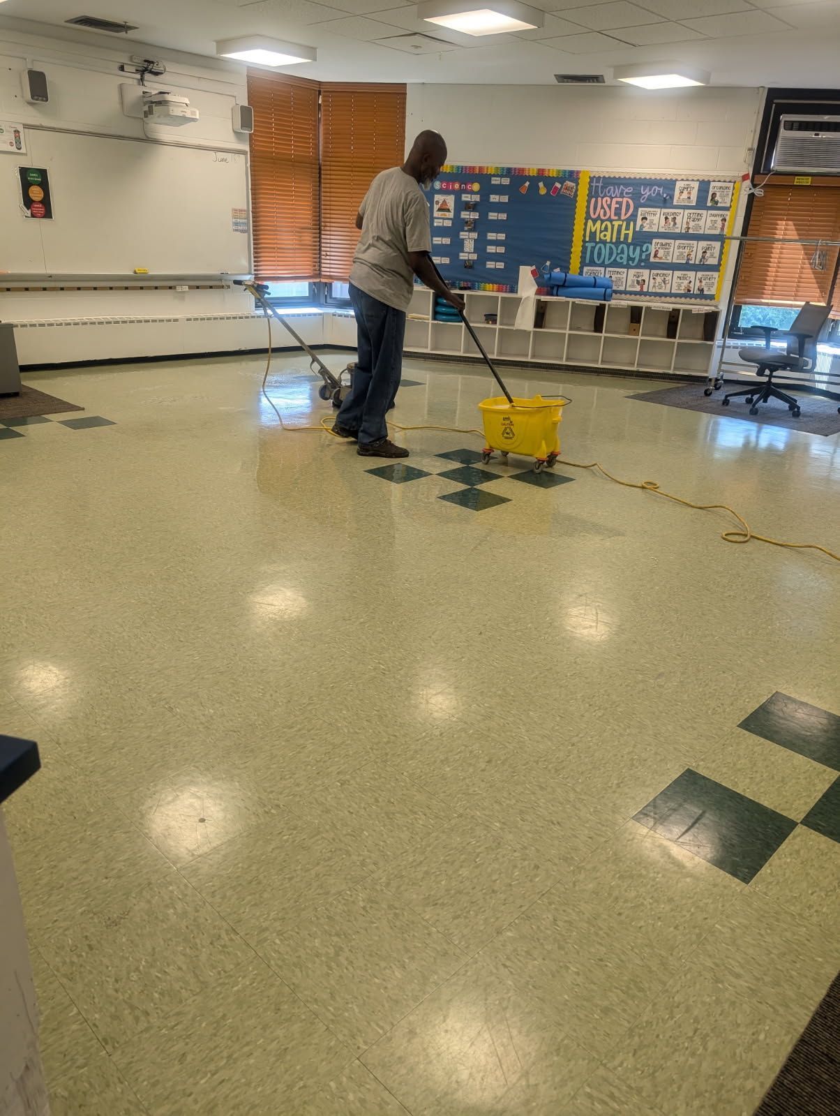 Person mopping a wet school classroom floor beside a yellow caution bucket.