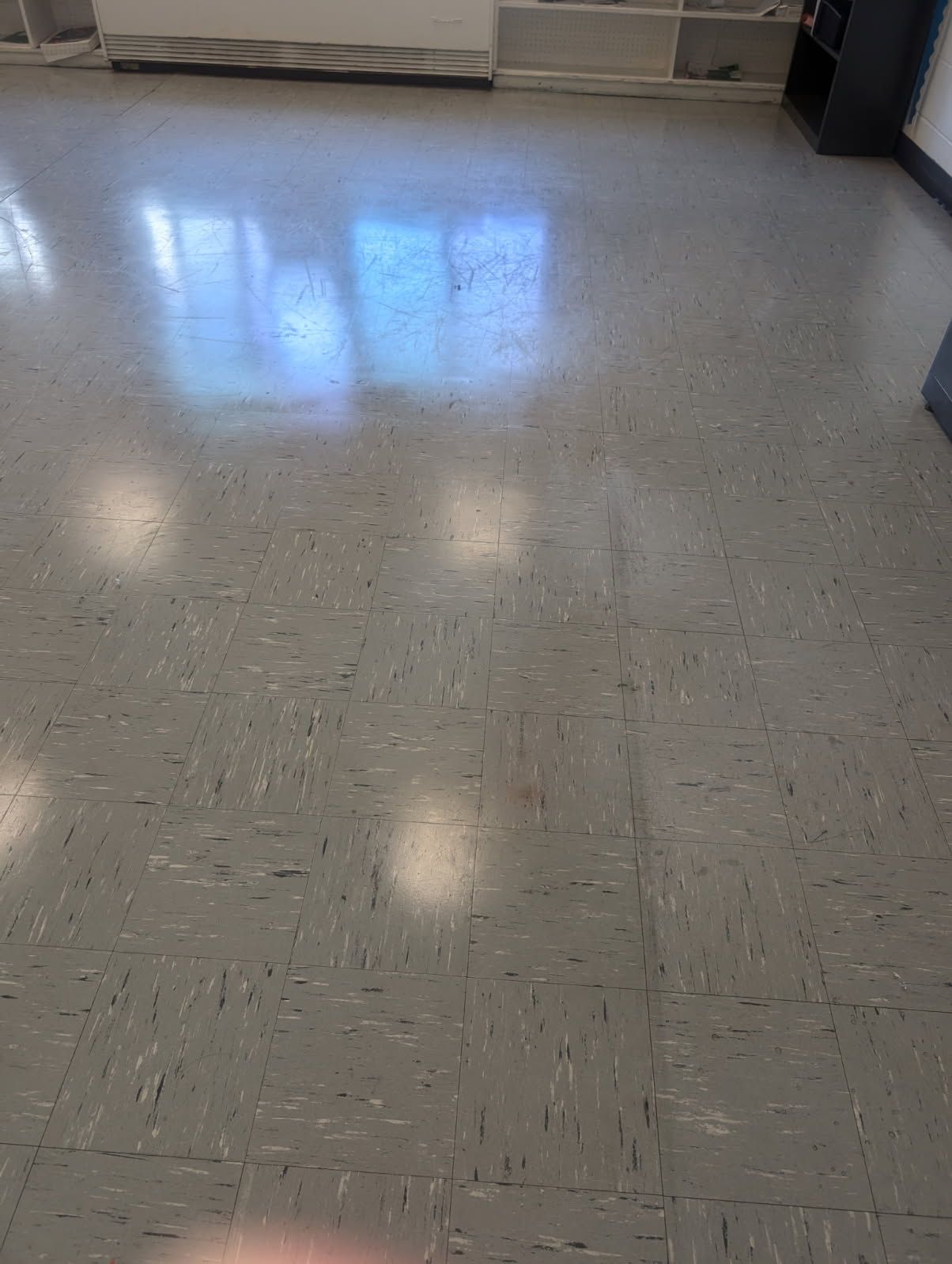 Empty tiled hallway floor with reflections from windows and wall baseboard heater.