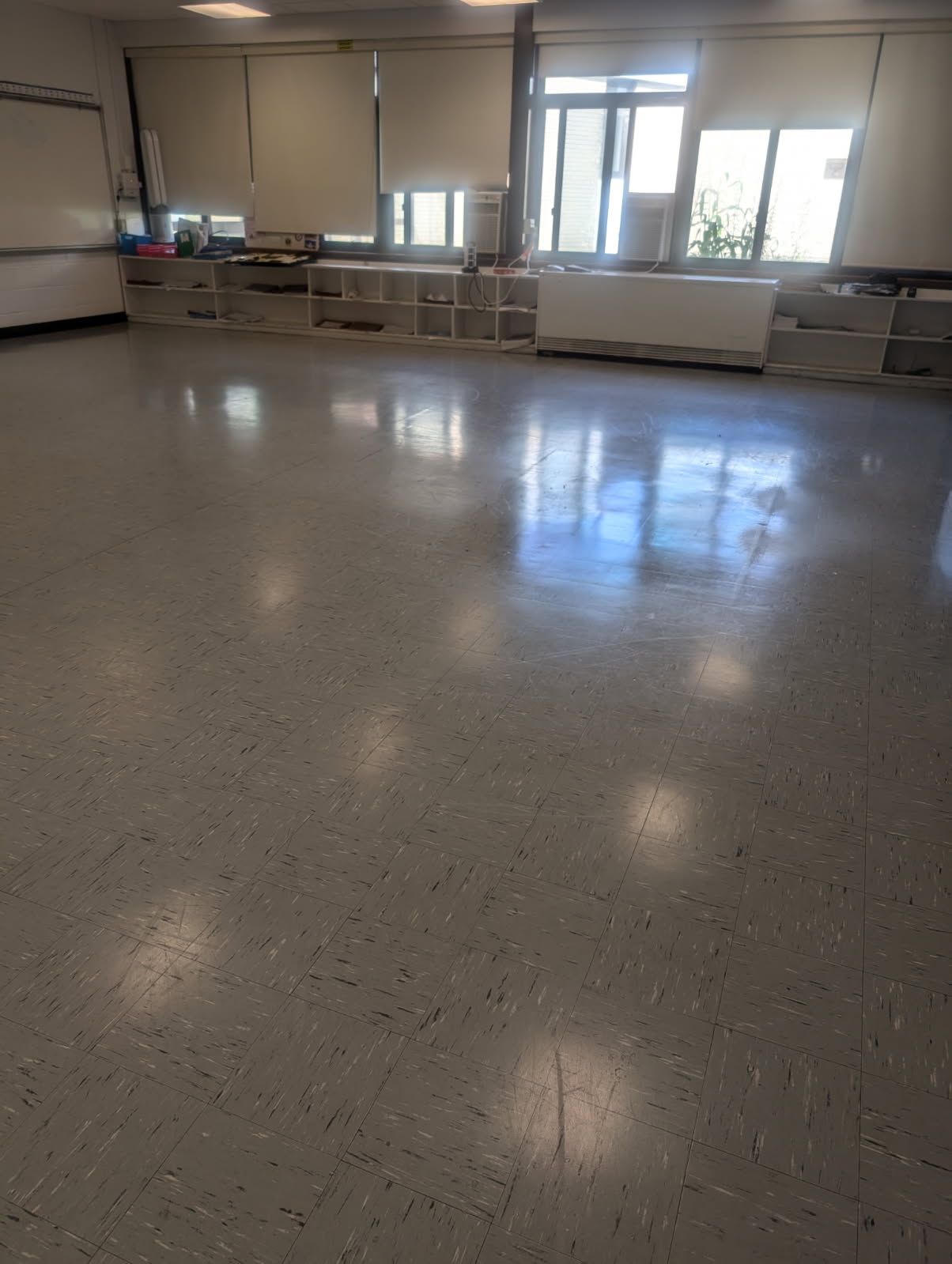Empty classroom with polished floor, windows, and tables along the back wall