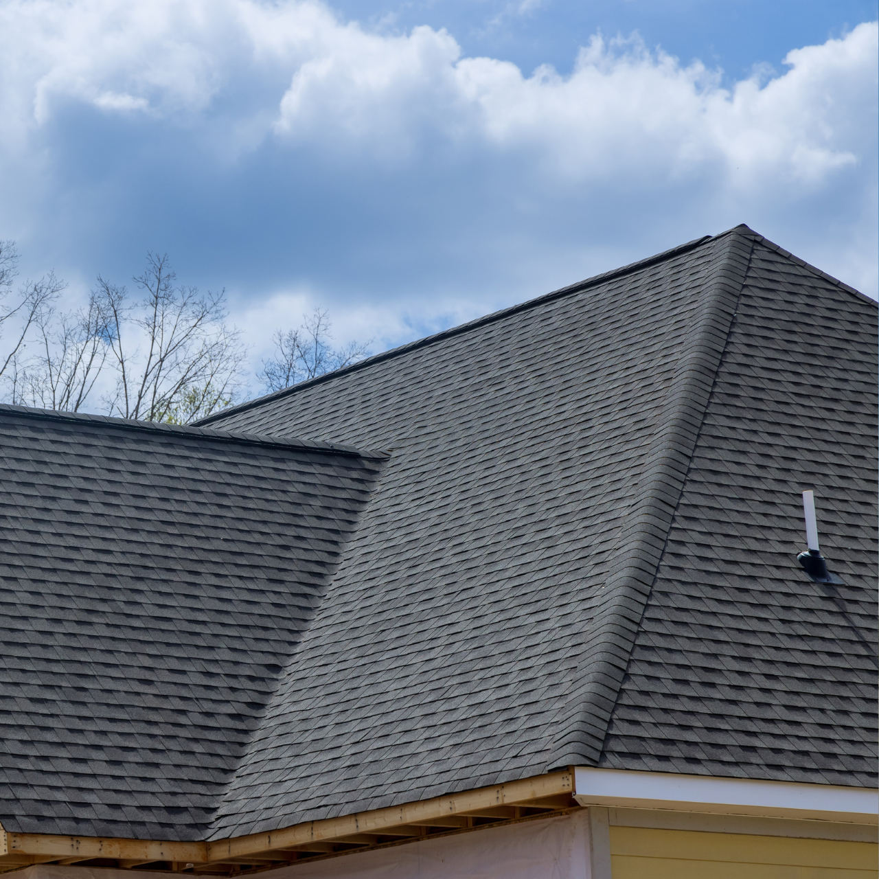 A multi-faceted gray shingled roof under a bright blue sky with clouds.