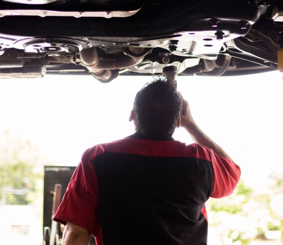 A man in a red and black shirt is working under a car
