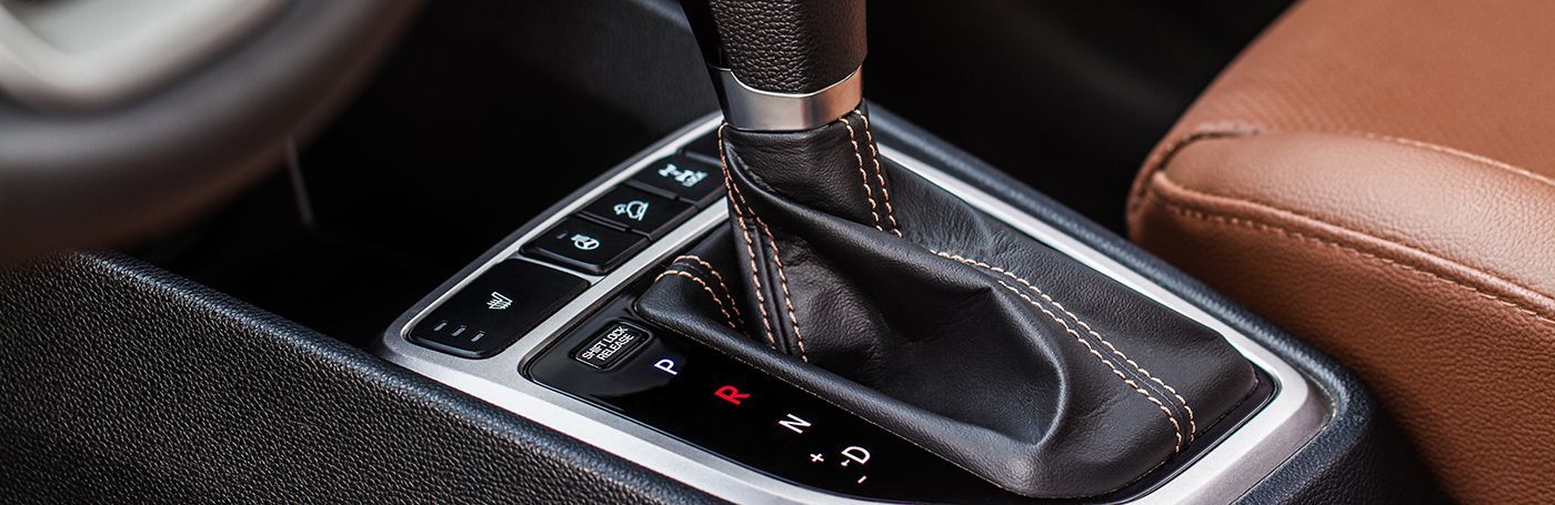 Close-up of a car's automatic gear shift lever, black leather with silver trim, brown leather seat.