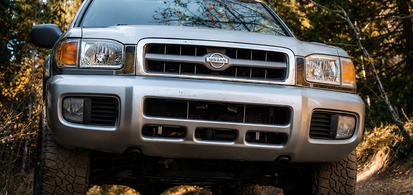 Front view of a silver SUV driving on a dirt road in a wooded area