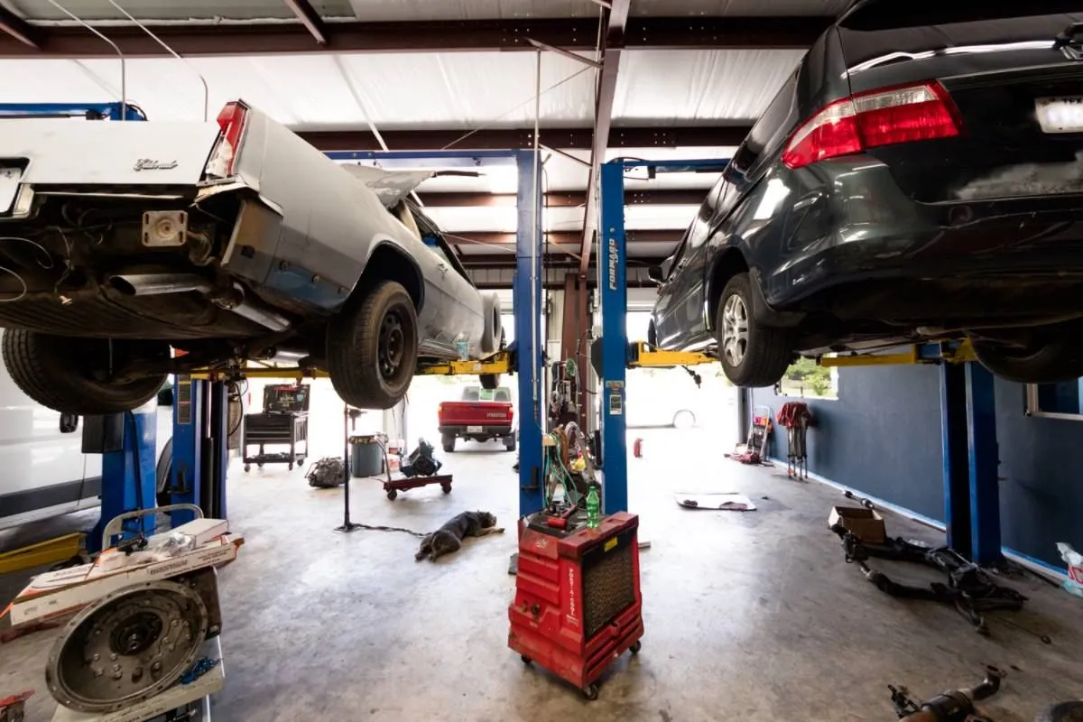 A bright auto repair shop with two cars raised on hydraulic lifts and a red toolbox in the center.