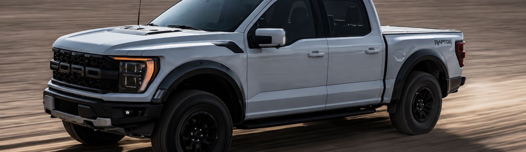 Silver pickup truck driving on a sandy surface near water at sunset