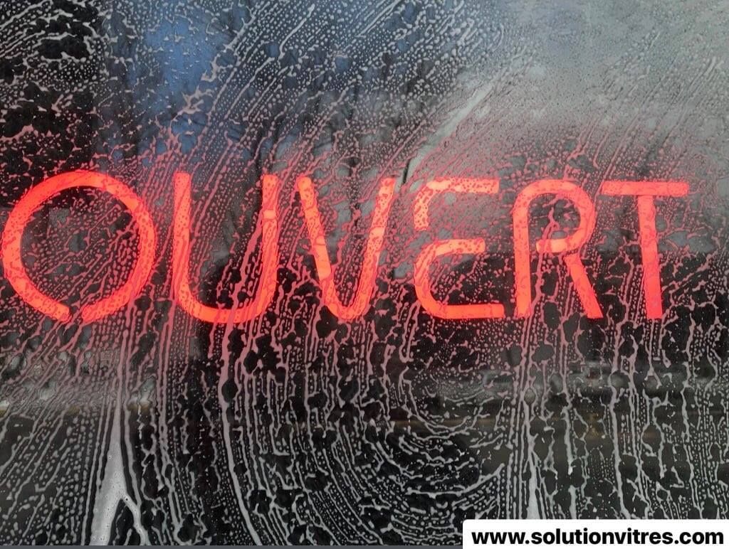 Enseigne lumineuse rouge « OUVERT » derrière une vitre mouillée avec des gouttelettes d'eau.