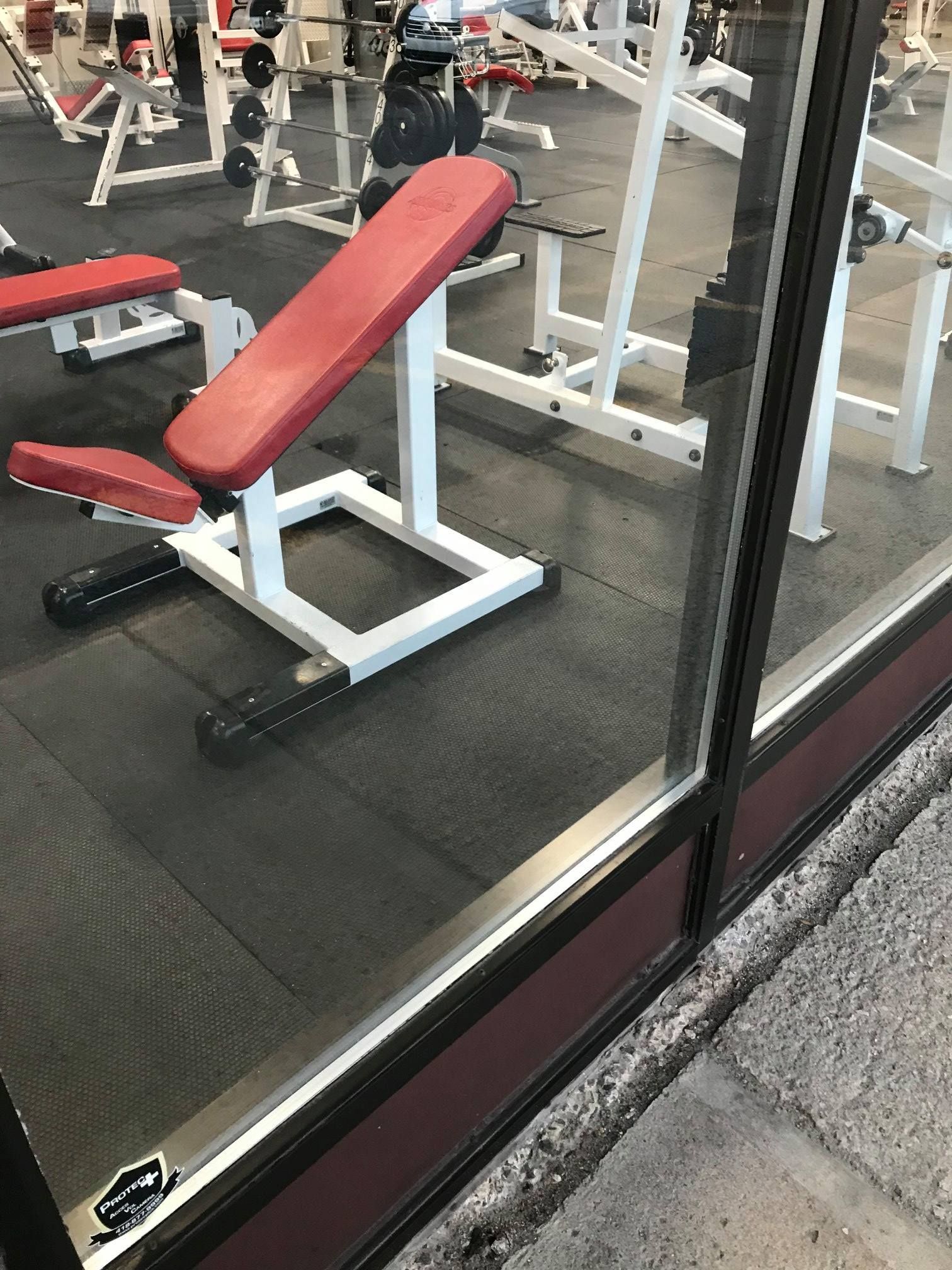 Banc incliné rouge dans une salle de sport avec sol noir et machines de musculation en arrière-plan.