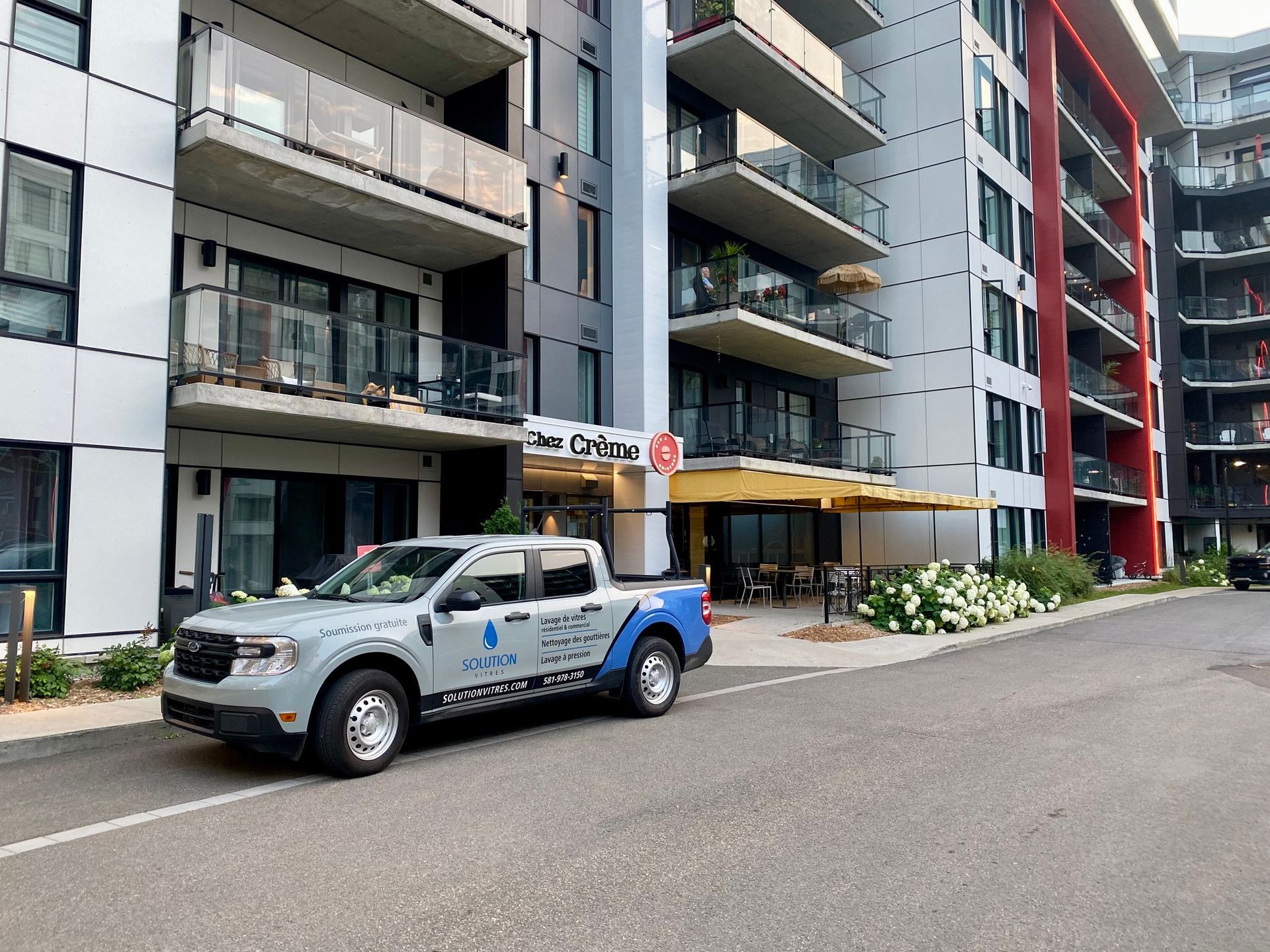 Une camionnette argentée et bleue garée devant des immeubles d'appartements modernes dans une rue de la ville