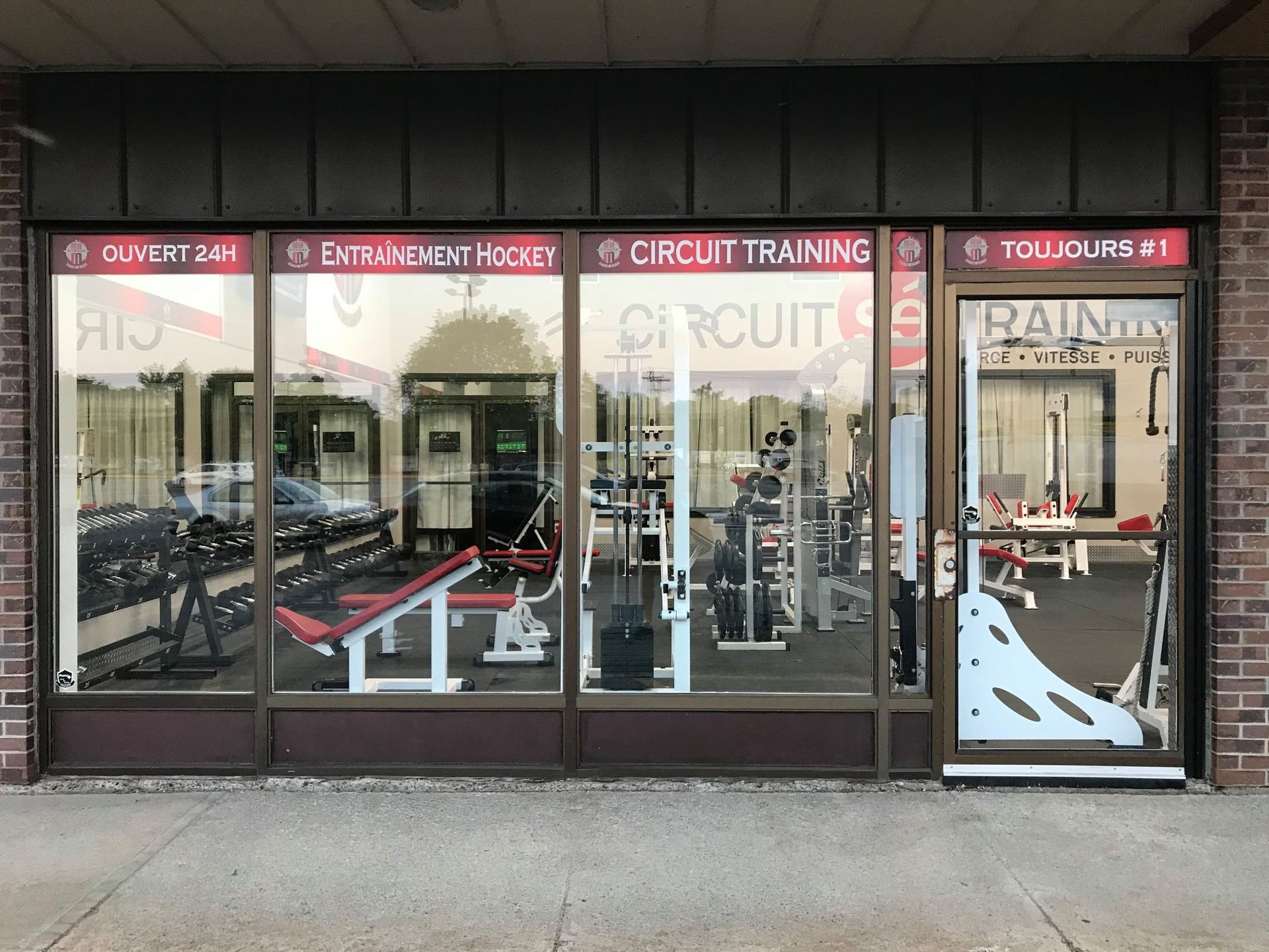 Façade extérieure d'une salle de sport spécialisée dans l'entraînement en circuit, avec de grandes vitrines et une enseigne rouge.