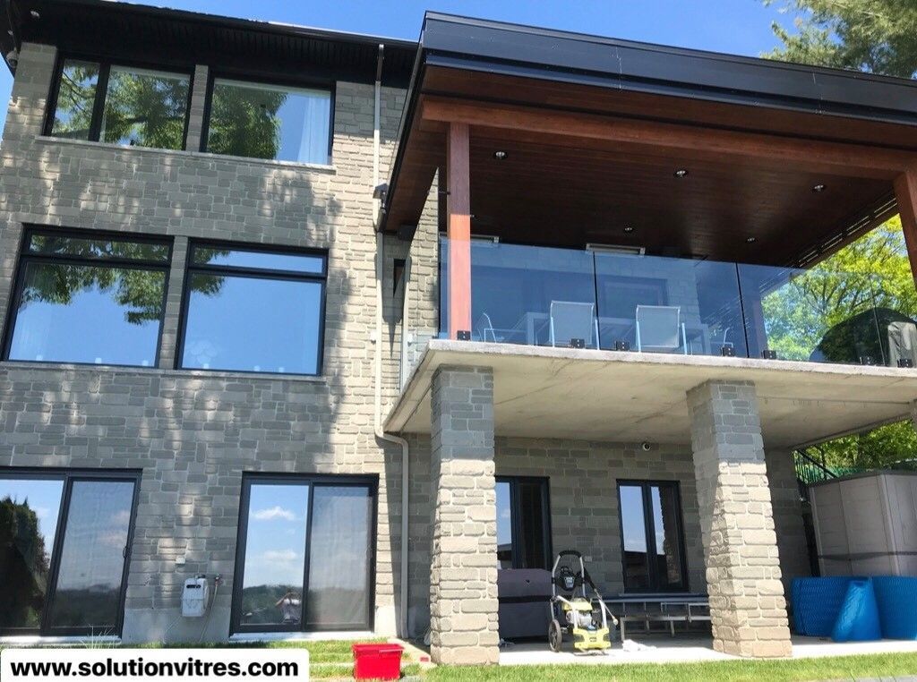 Maison moderne de deux étages en pierre et bois avec de grandes fenêtres et un balcon couvert