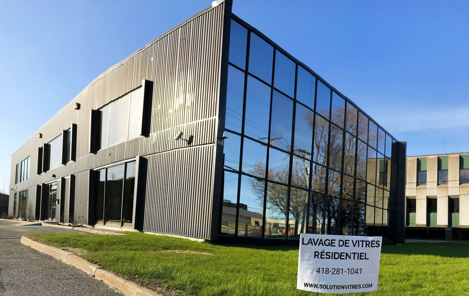 Immeuble de bureaux moderne avec fenêtres réfléchissantes et pelouse, avec un panneau indiquant « Lange de Vivre Résidentiel »