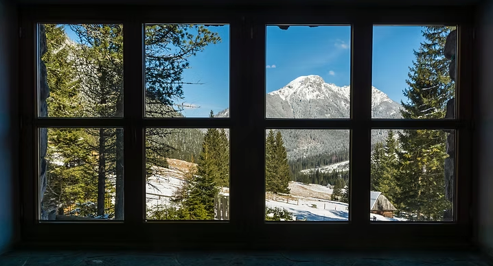 Montagnes enneigées et pins aperçus à travers la grille sombre d'une fenêtre.