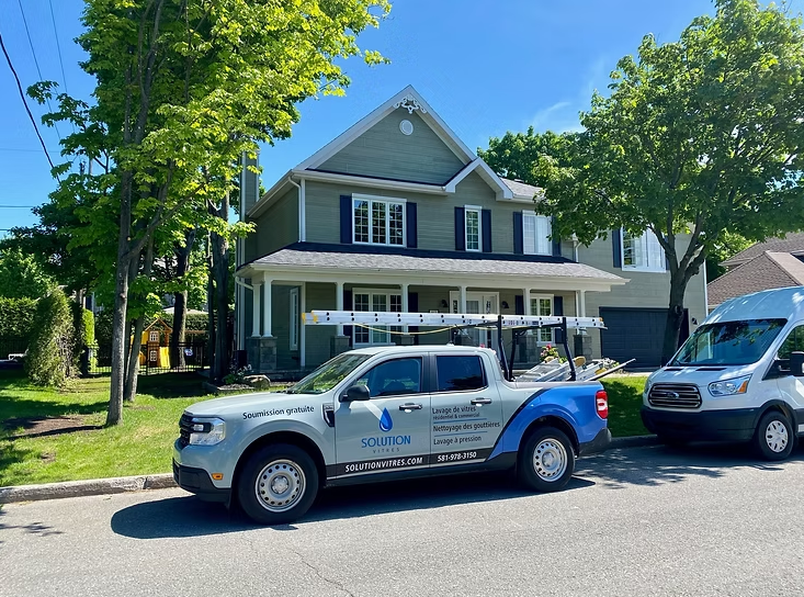 Deux fourgonnettes utilitaires blanches étaient garées devant une maison grise avec un porche, dans une rue bordée d'arbres.