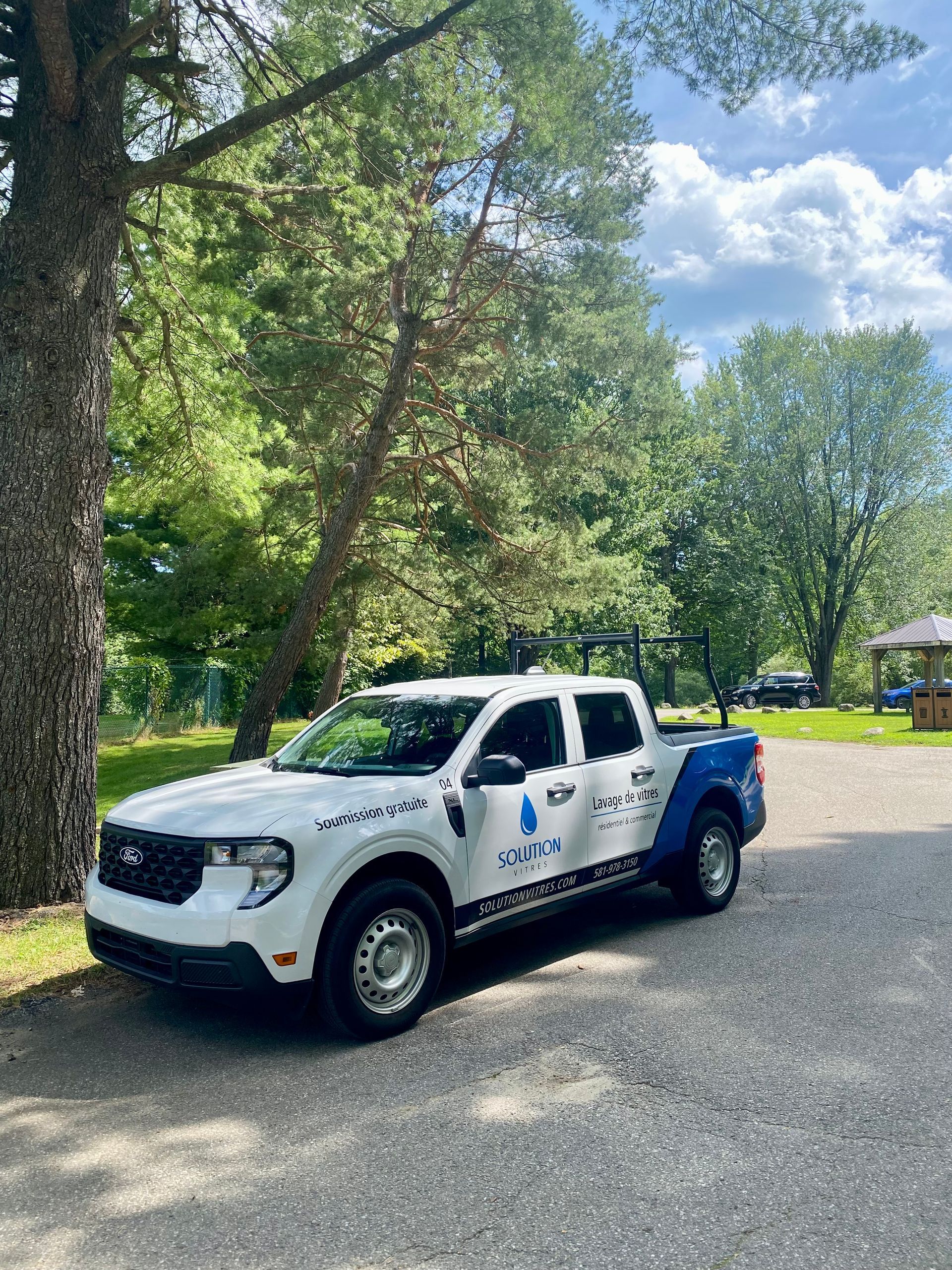 Camion utilitaire blanc et bleu stationné sur une route bordée d'arbres dans un parc ensoleillé