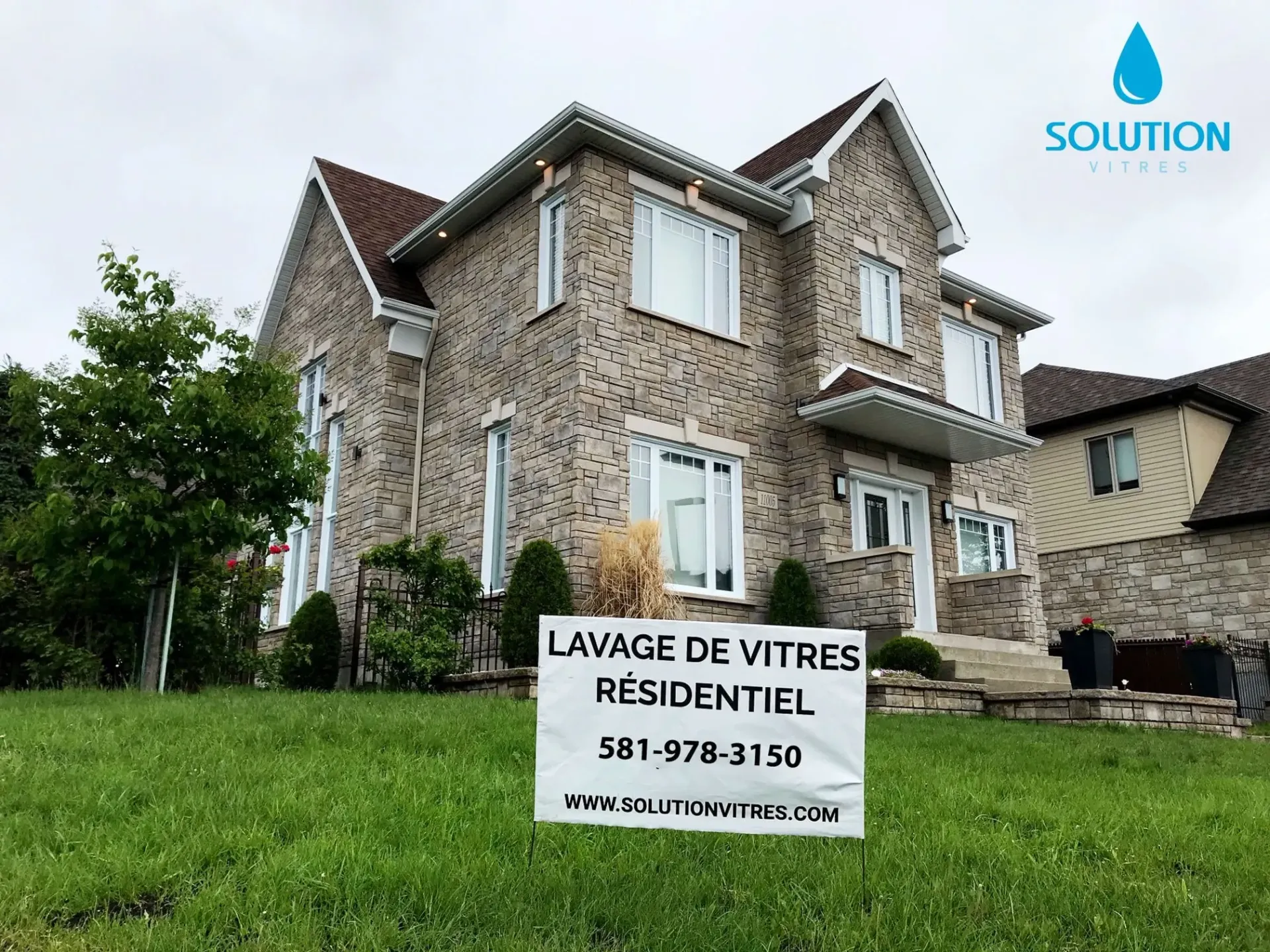 Maison en pierre avec une pancarte indiquant « Lavage de vitres résidentiel » et un logo « Solution » sur la pelouse.