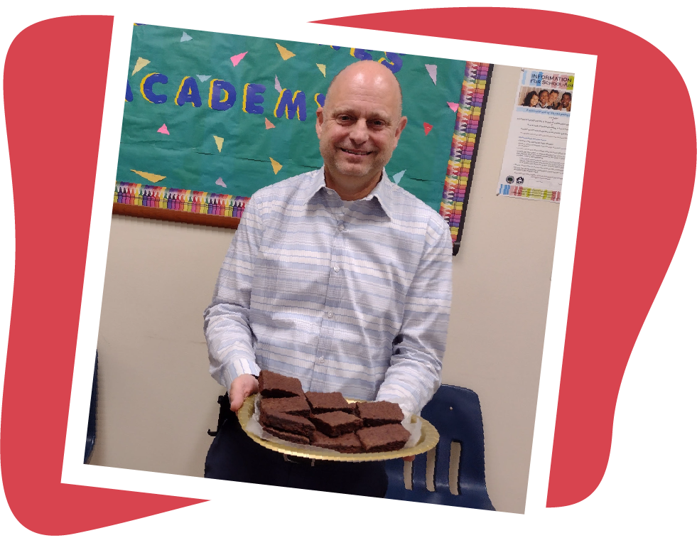 Man holding a plate of brownies, smiling indoors near a bulletin board.