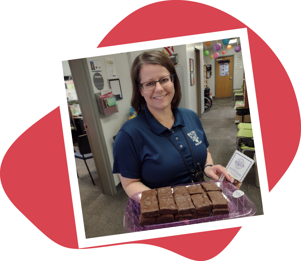 Woman in blue shirt holding tray of brownies, smiling inside.