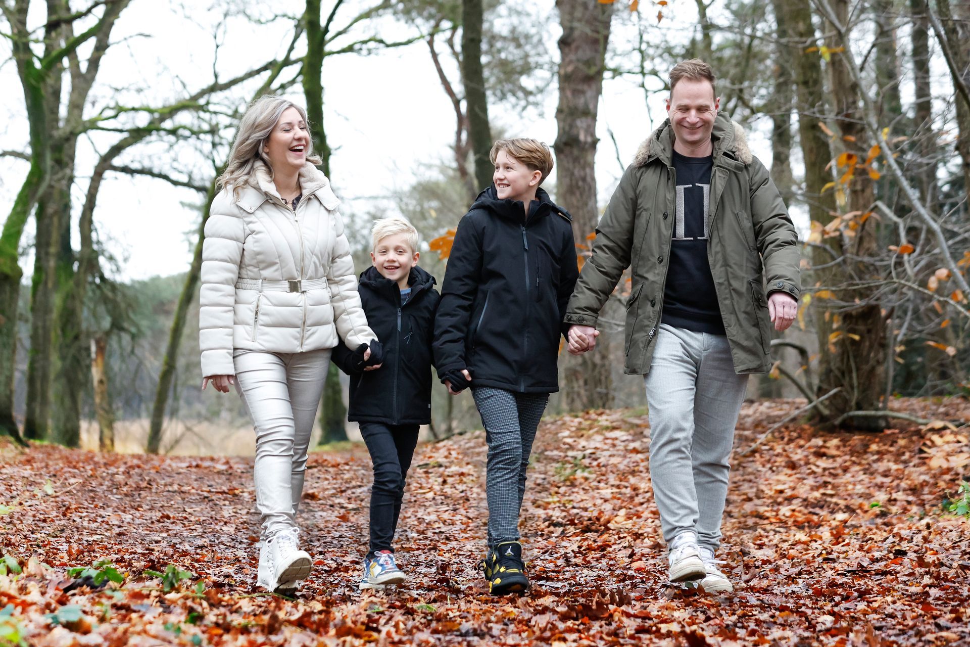 Een gezin loopt hand in hand door het bos.