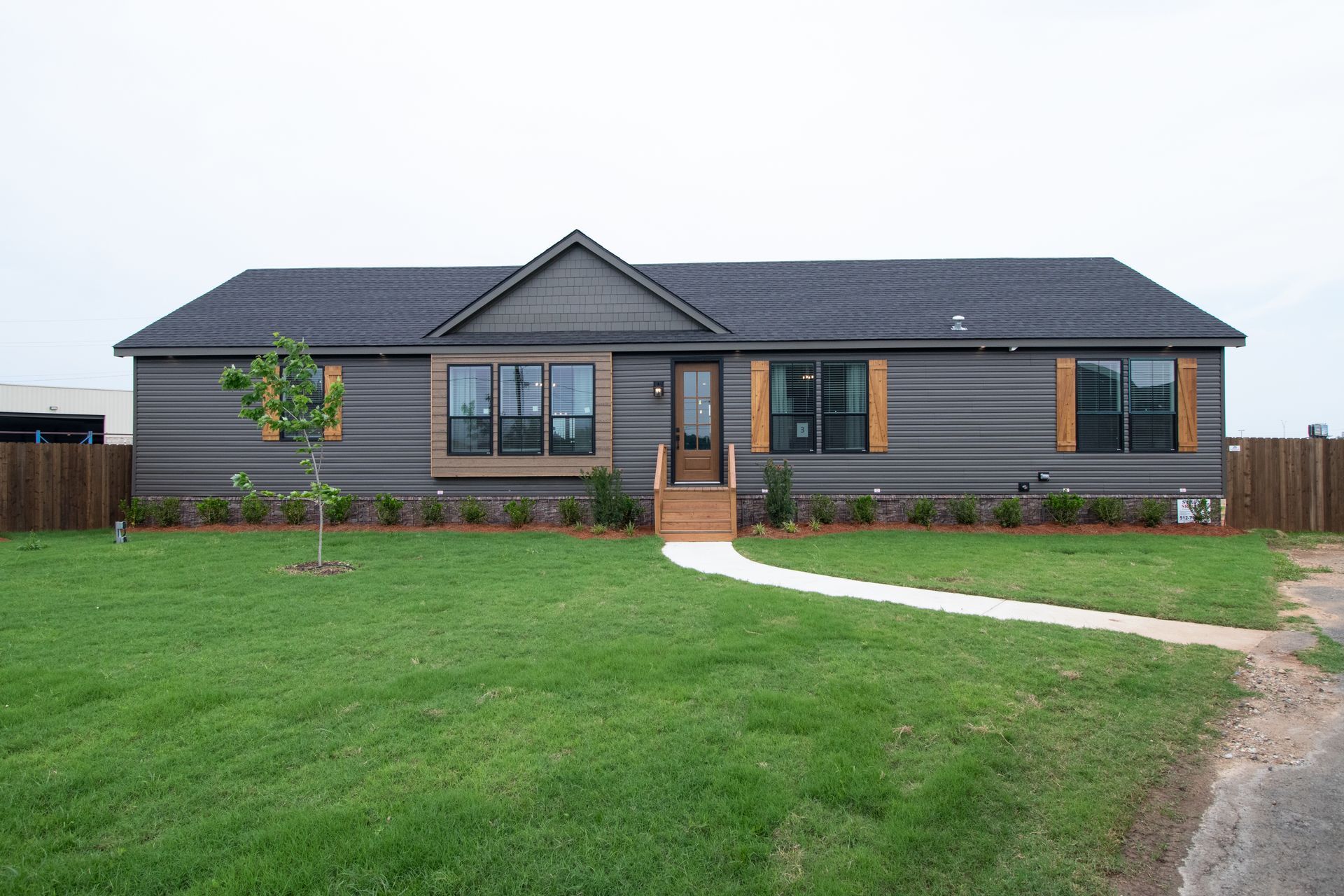 Single-story dark gray house with a large green lawn and a white walkway to the front door.