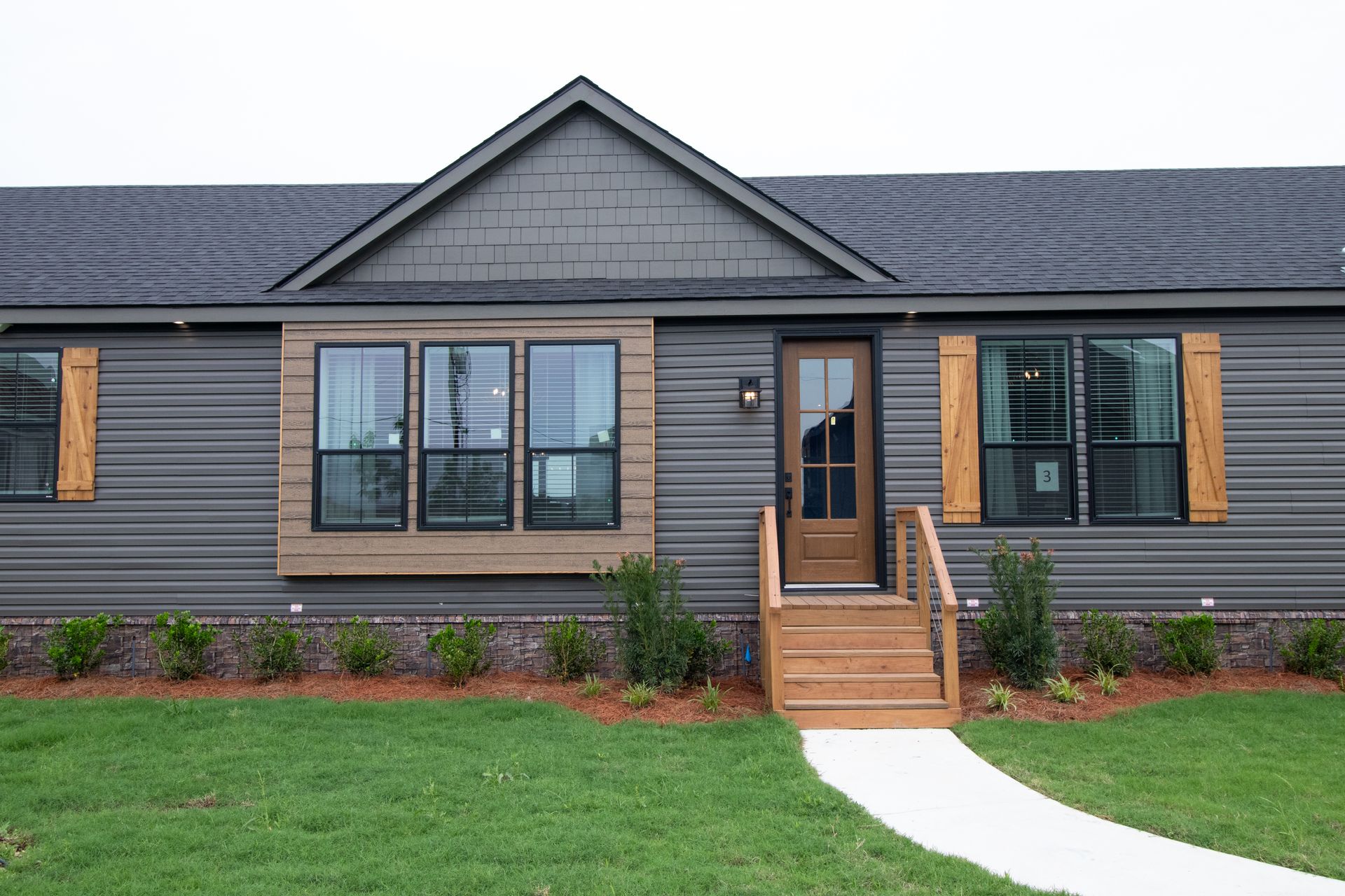 Front view of a gray single-story house with wood accents, central stairs, and a green lawn.