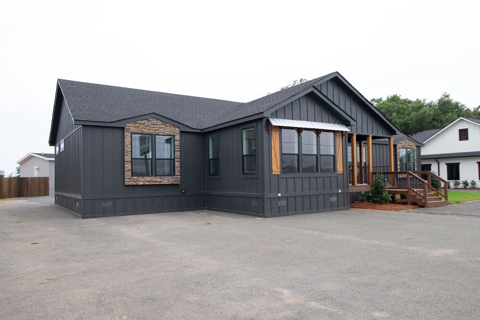 Dark gray house with a gabled roof and front porch on a gravel lot