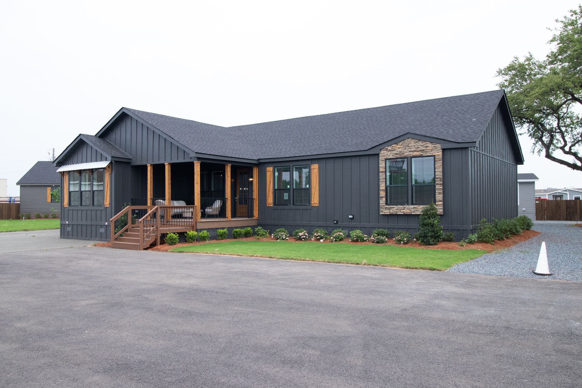 Dark gray single-story house with a covered porch and wooden steps on a gravel lot