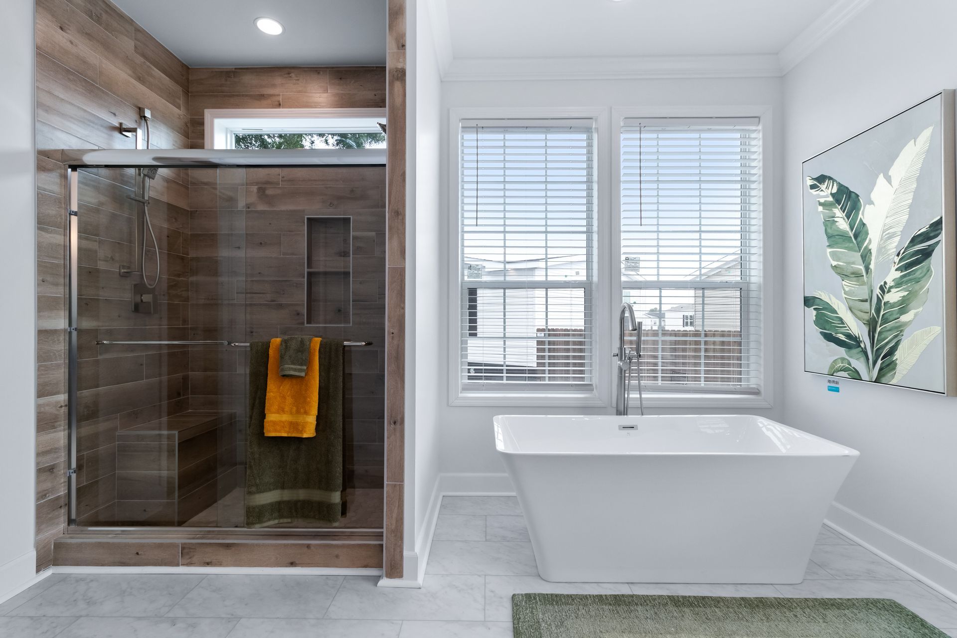 Modern bathroom with glass shower, freestanding tub, and window with white blinds