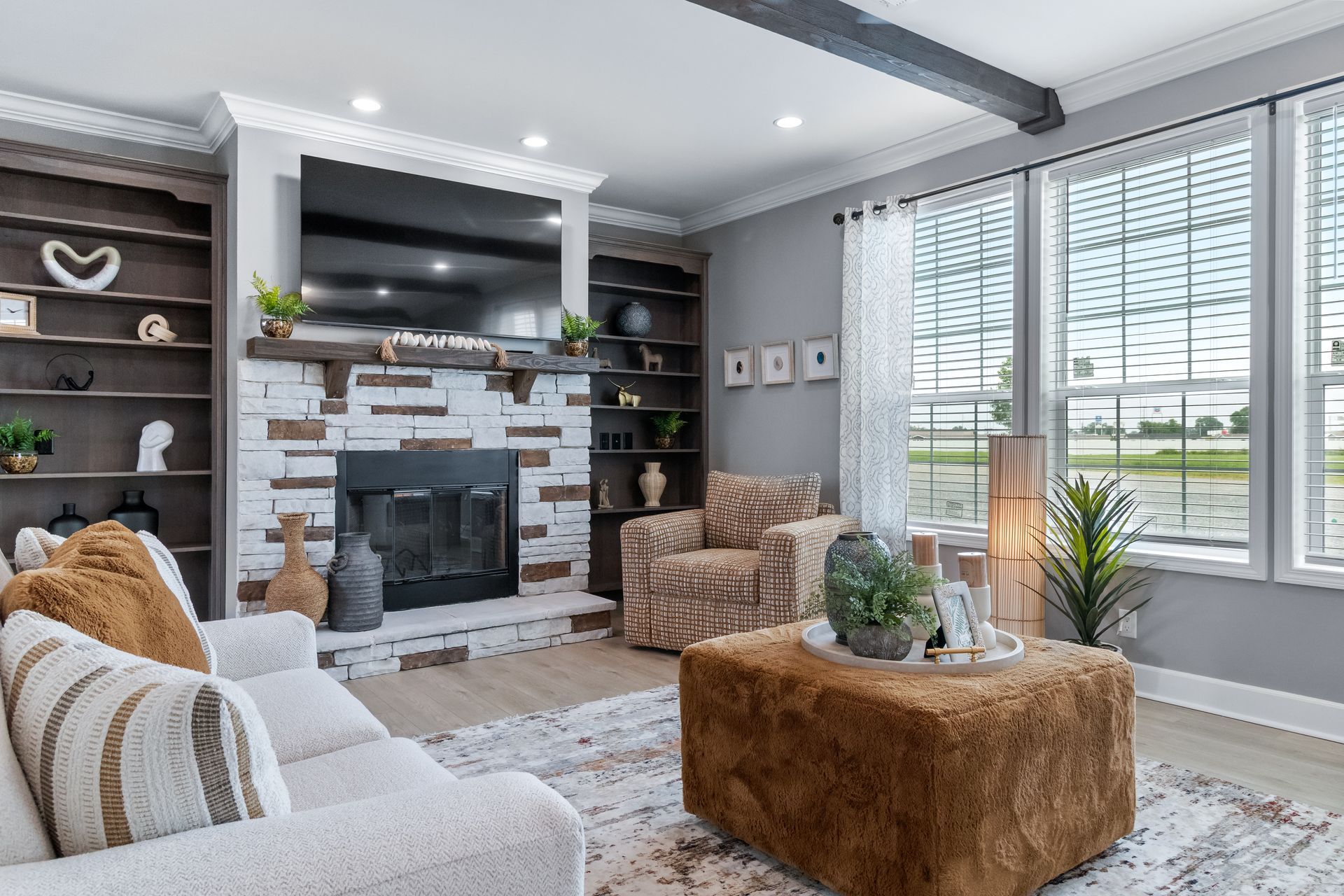 Bright living room with fireplace, gray walls, white shutters, and tan accent chairs by large windows