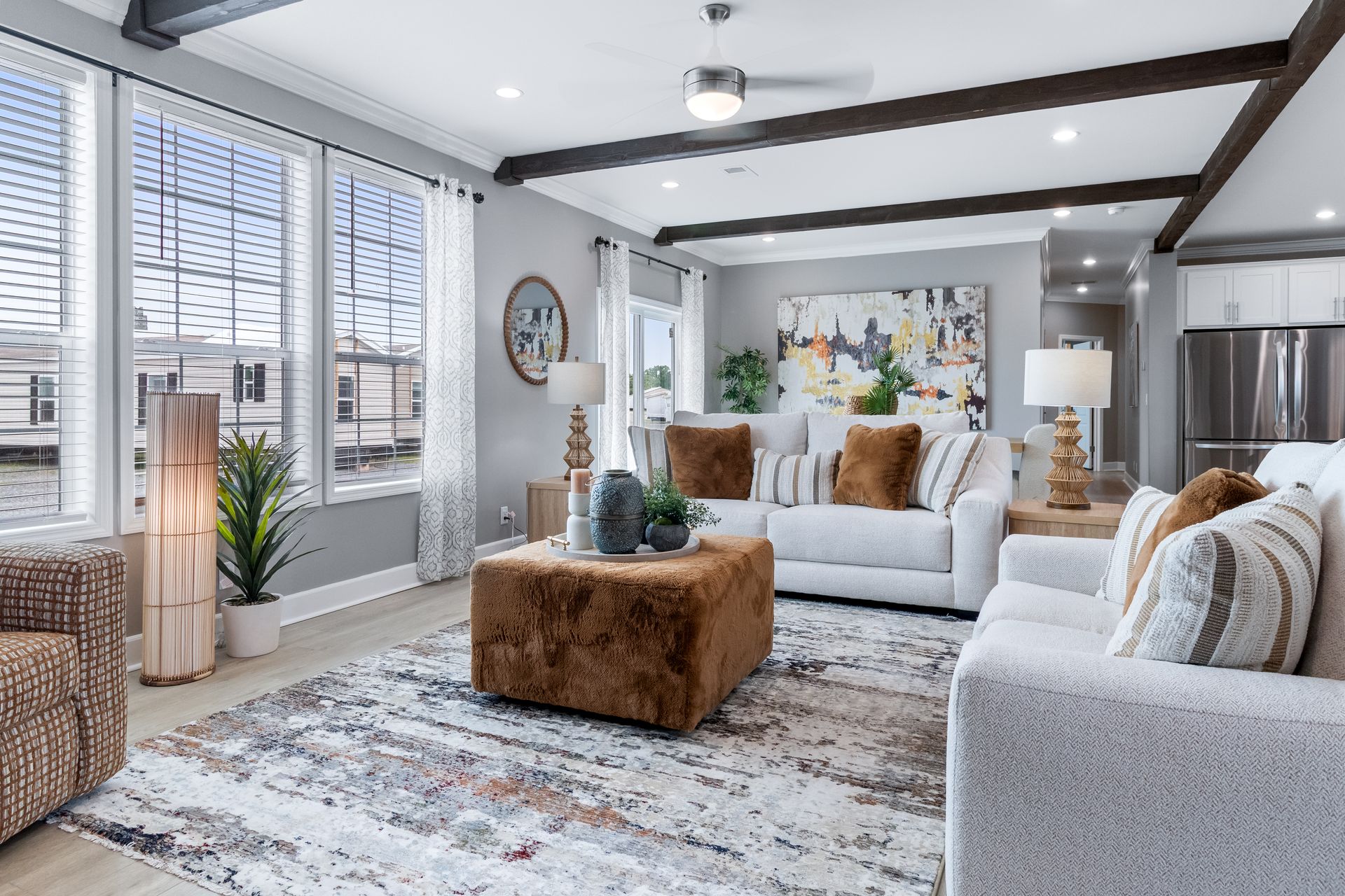 Bright living room with gray sofas, patterned rug, wood beams, and large windows overlooking city buildings