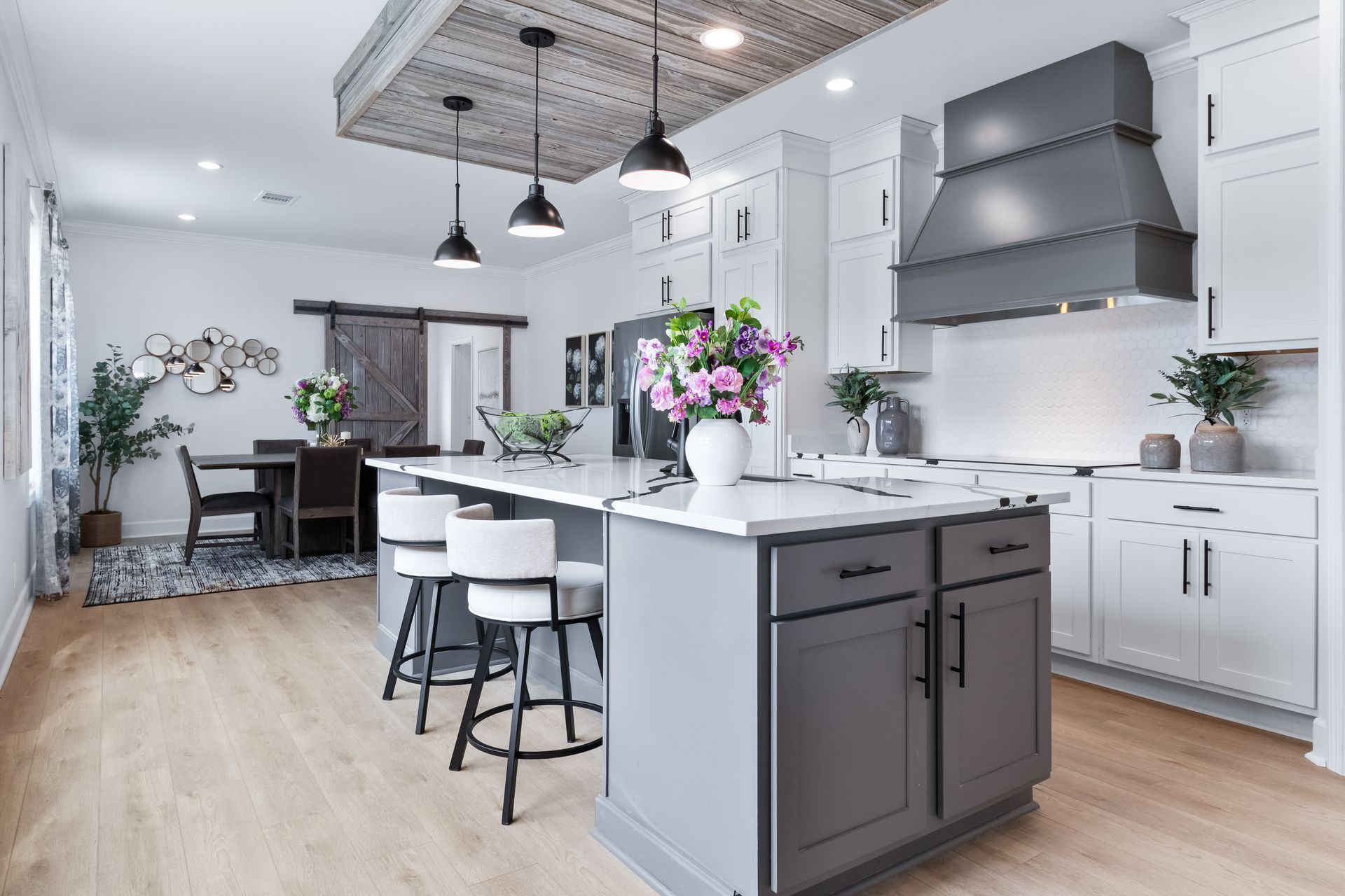 Bright modern kitchen with white cabinets, gray island, pendant lights, and flowers on the counter