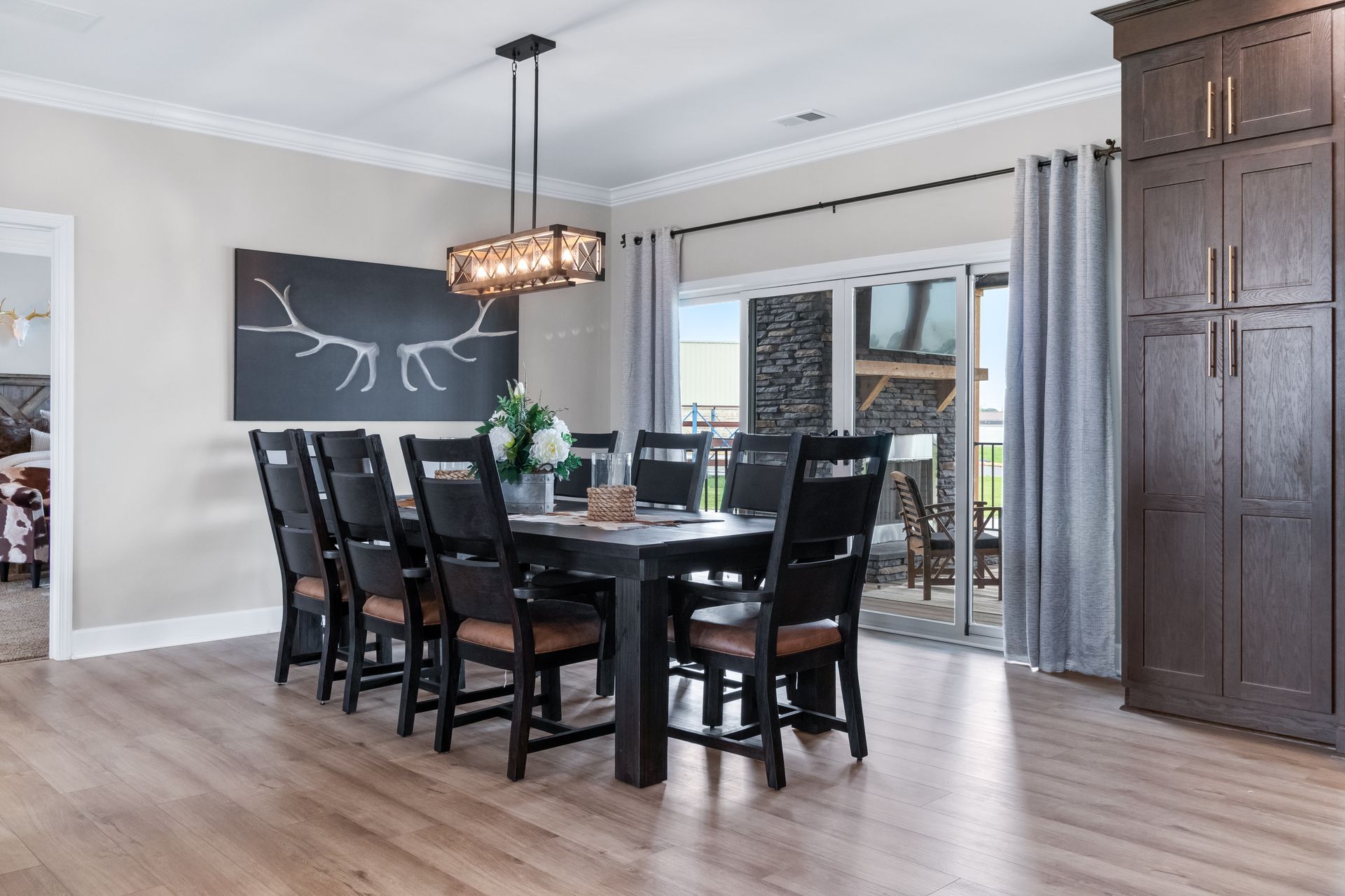 Modern dining room with black table and chairs, large wall art, chandelier, and sliding glass doors.