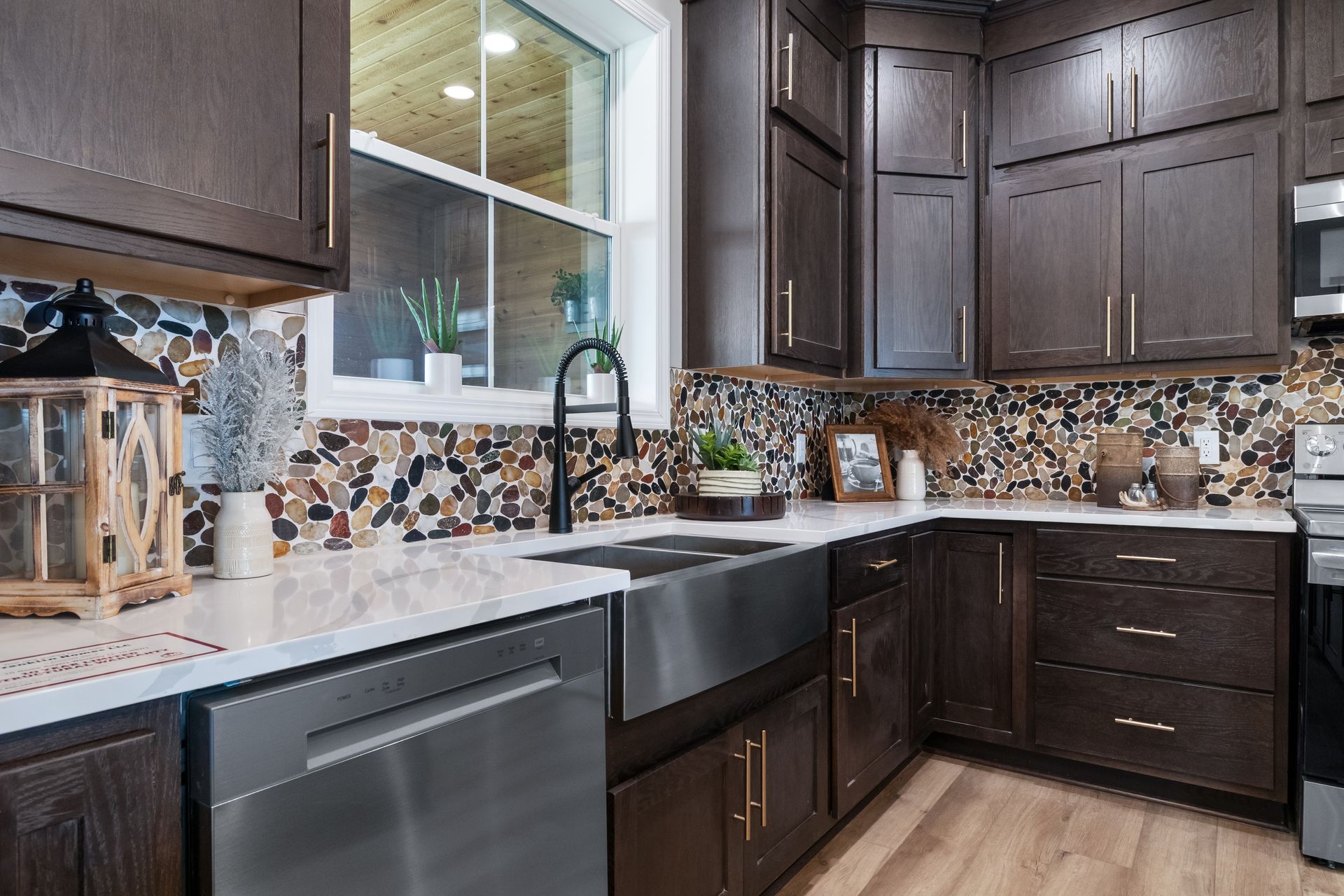 Modern kitchen with dark wood cabinets, mosaic backsplash, stainless sink, and dishwasher under a window