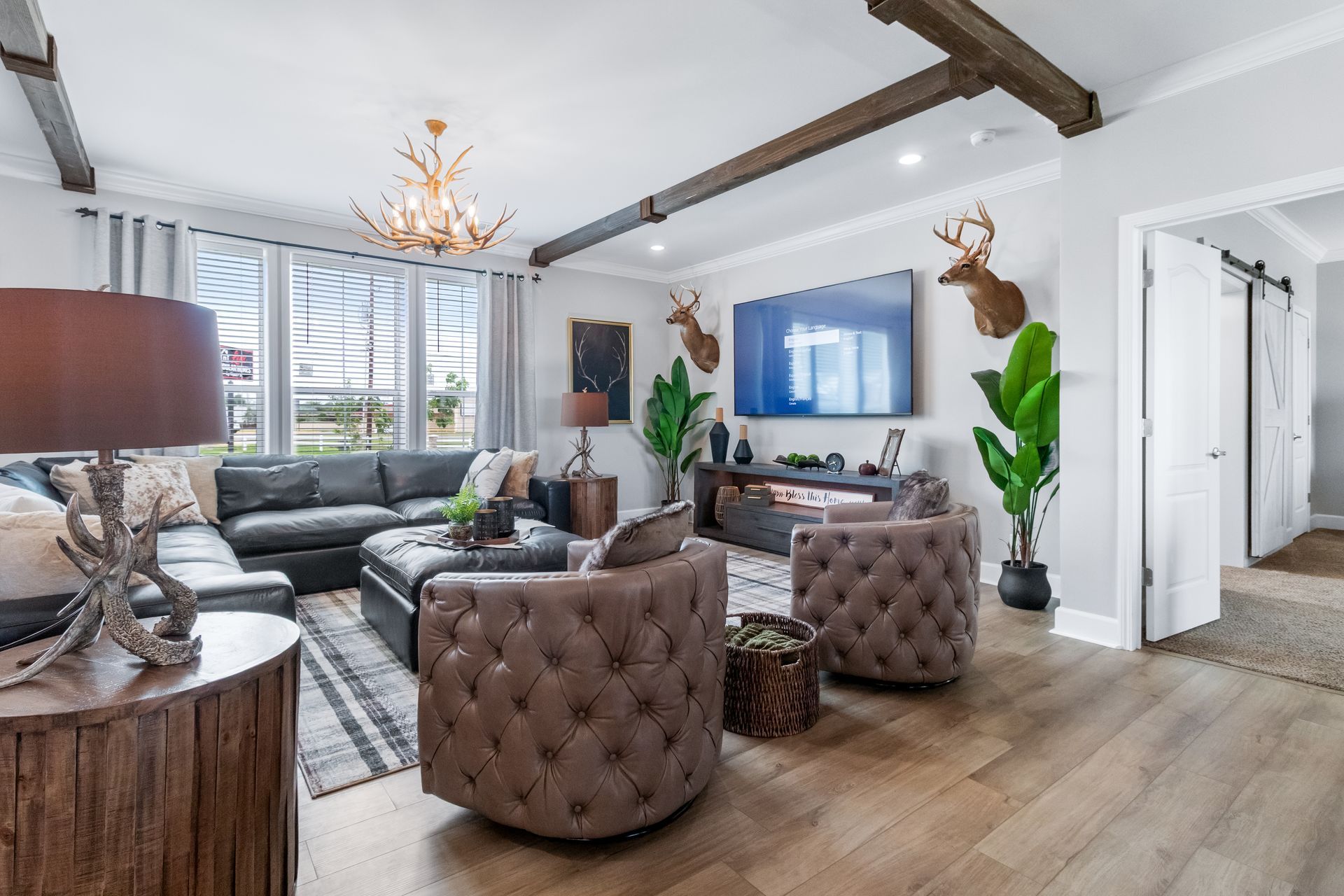Bright modern living room with gray sofas, tufted chairs, TV, wood beams, and large windows