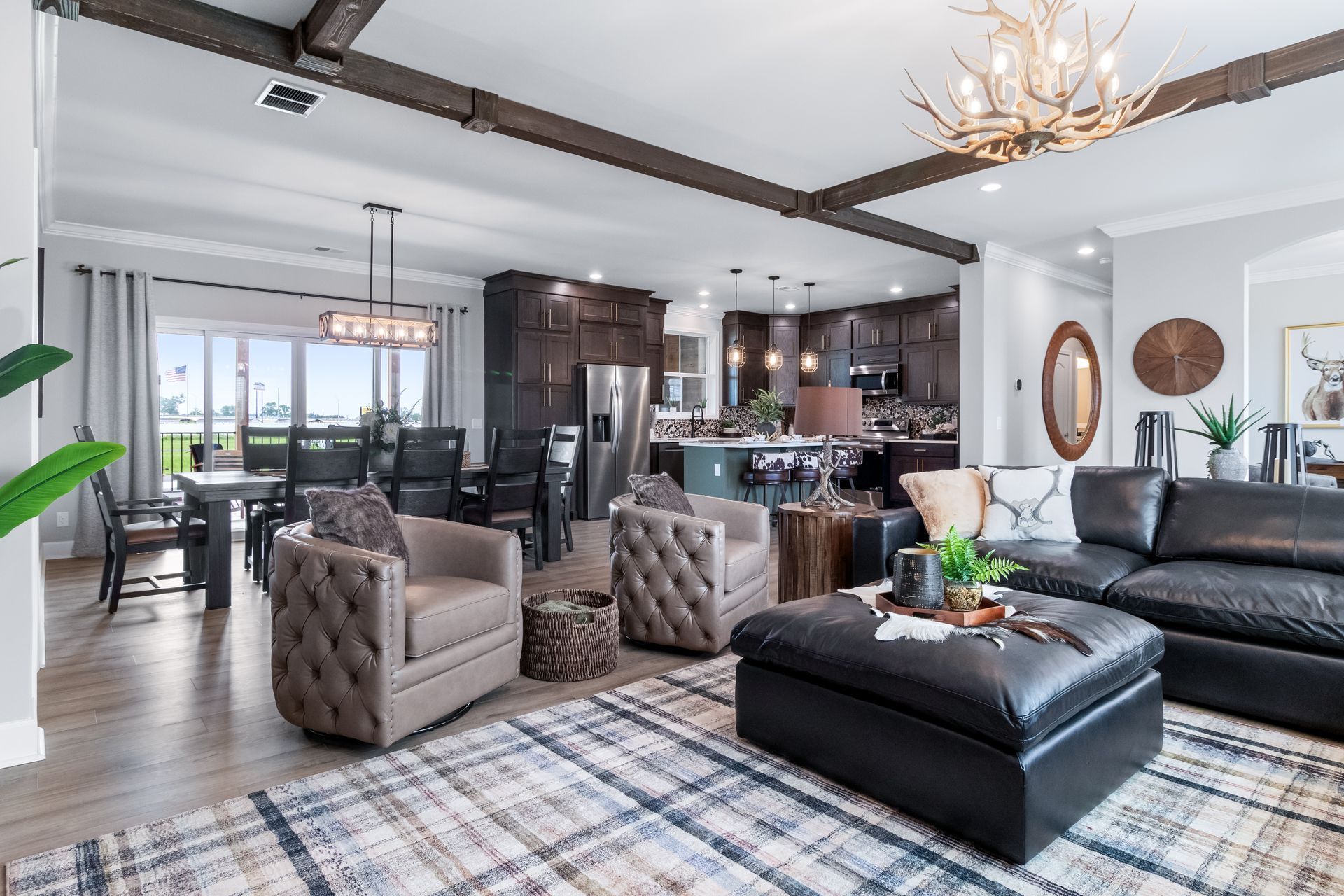 Modern open-plan living room with black leather sectional, patterned chairs, and dining area with dark wood accents.