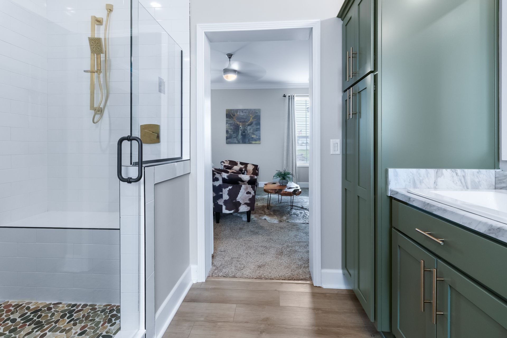 Bathroom doorway looking into a living room, with glass shower door, green vanity, and hardwood floor.