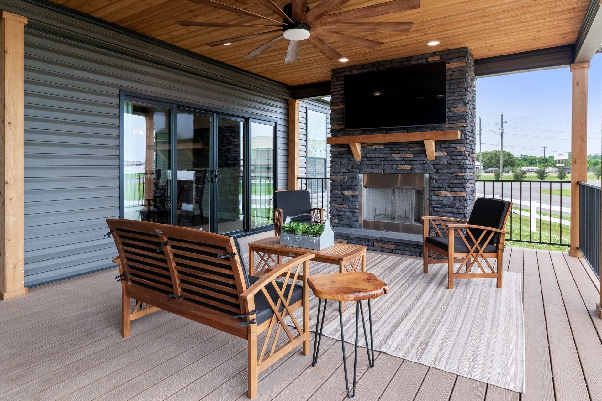Covered porch with wooden seating, stone fireplace, and TV overlooking a grassy landscape