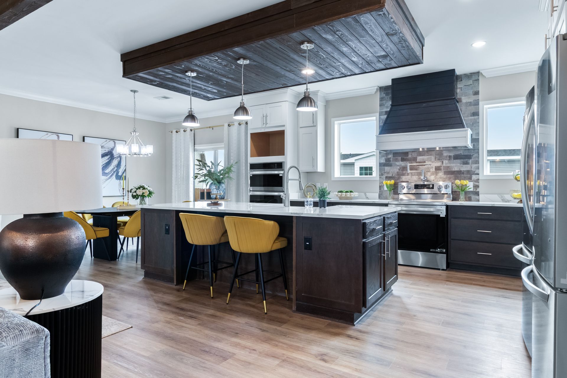 Modern open-concept kitchen with dark island, yellow stools, white cabinets, and exposed wood beams