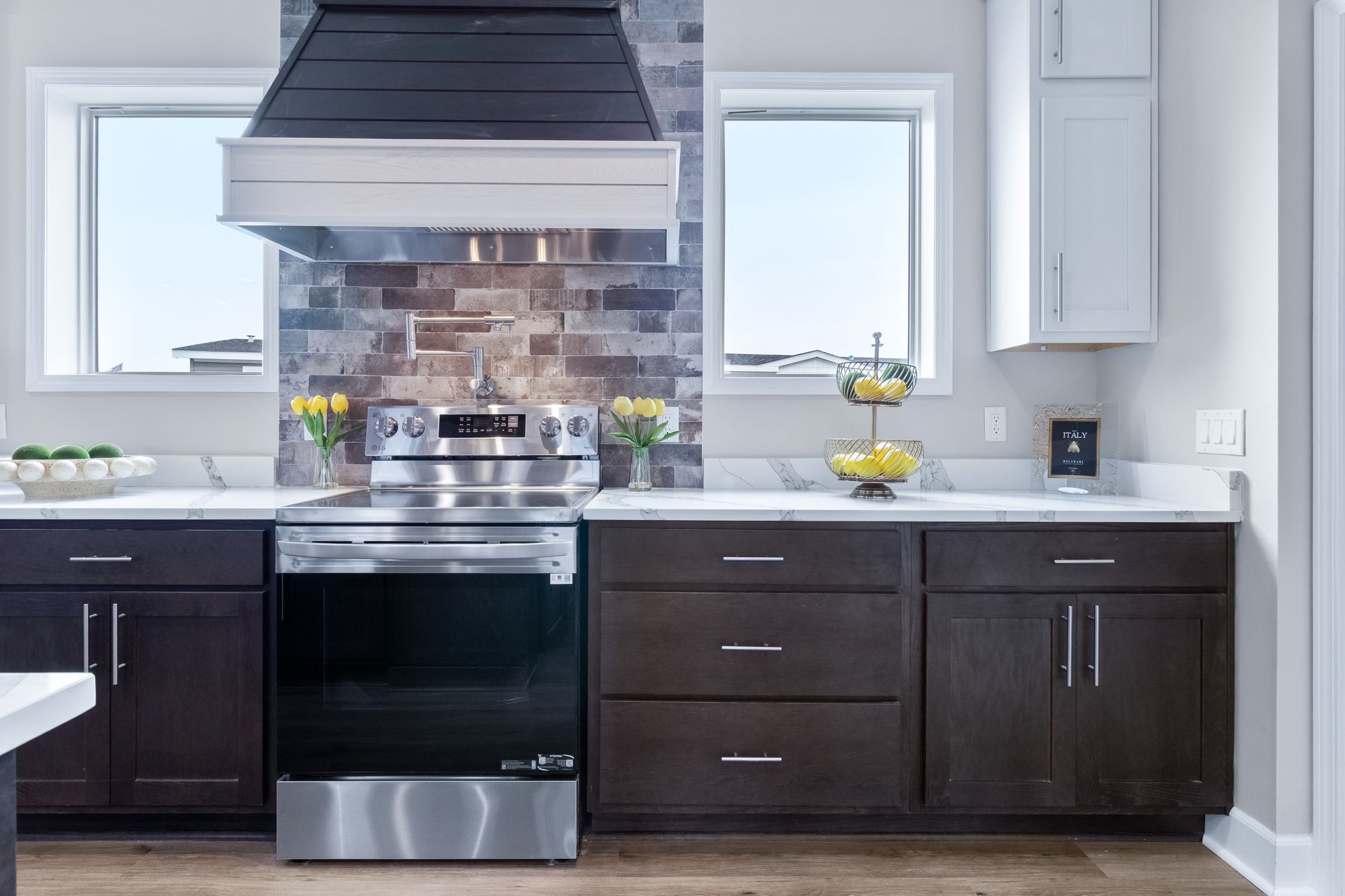 Modern kitchen with dark cabinets, stainless stove, large range hood, and white countertops