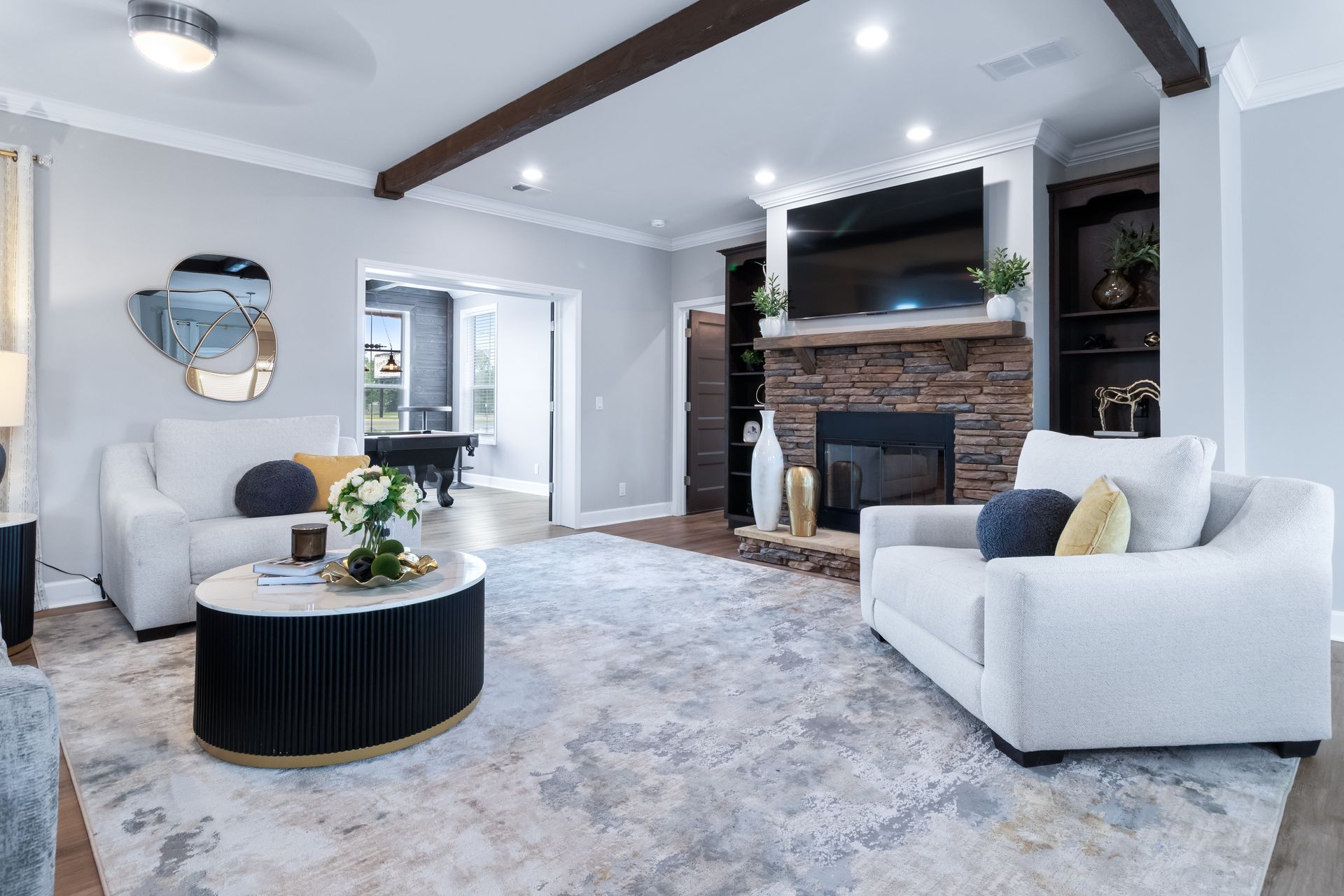 Bright living room with white sofas, black coffee table, stone fireplace, and wall-mounted TV