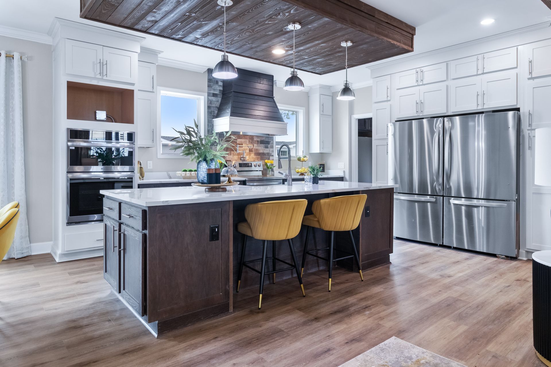 Modern kitchen with dark island, yellow stools, white cabinets, and stainless steel appliances