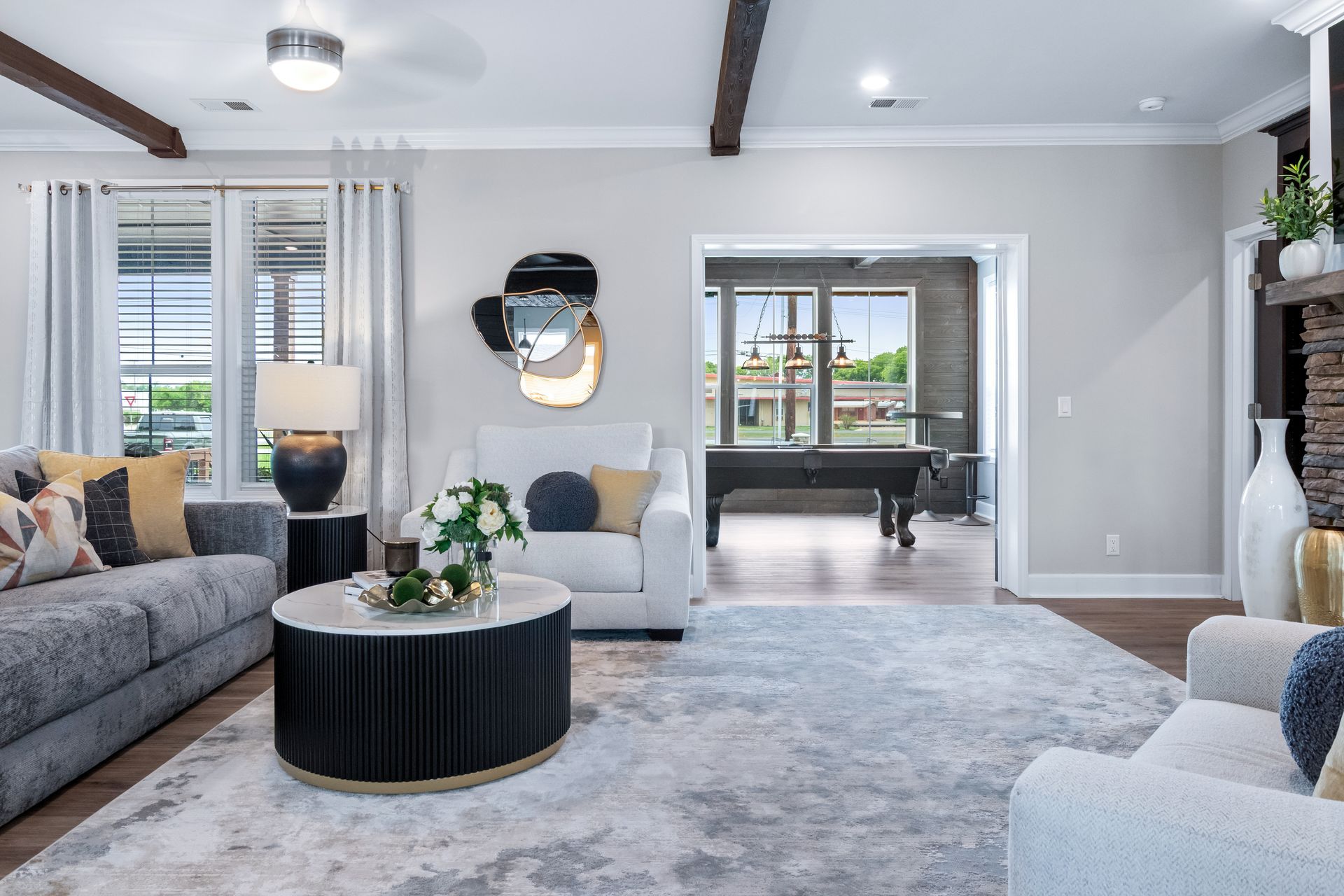 Bright modern living room with gray sofas, round coffee table, and large windows leading to another room