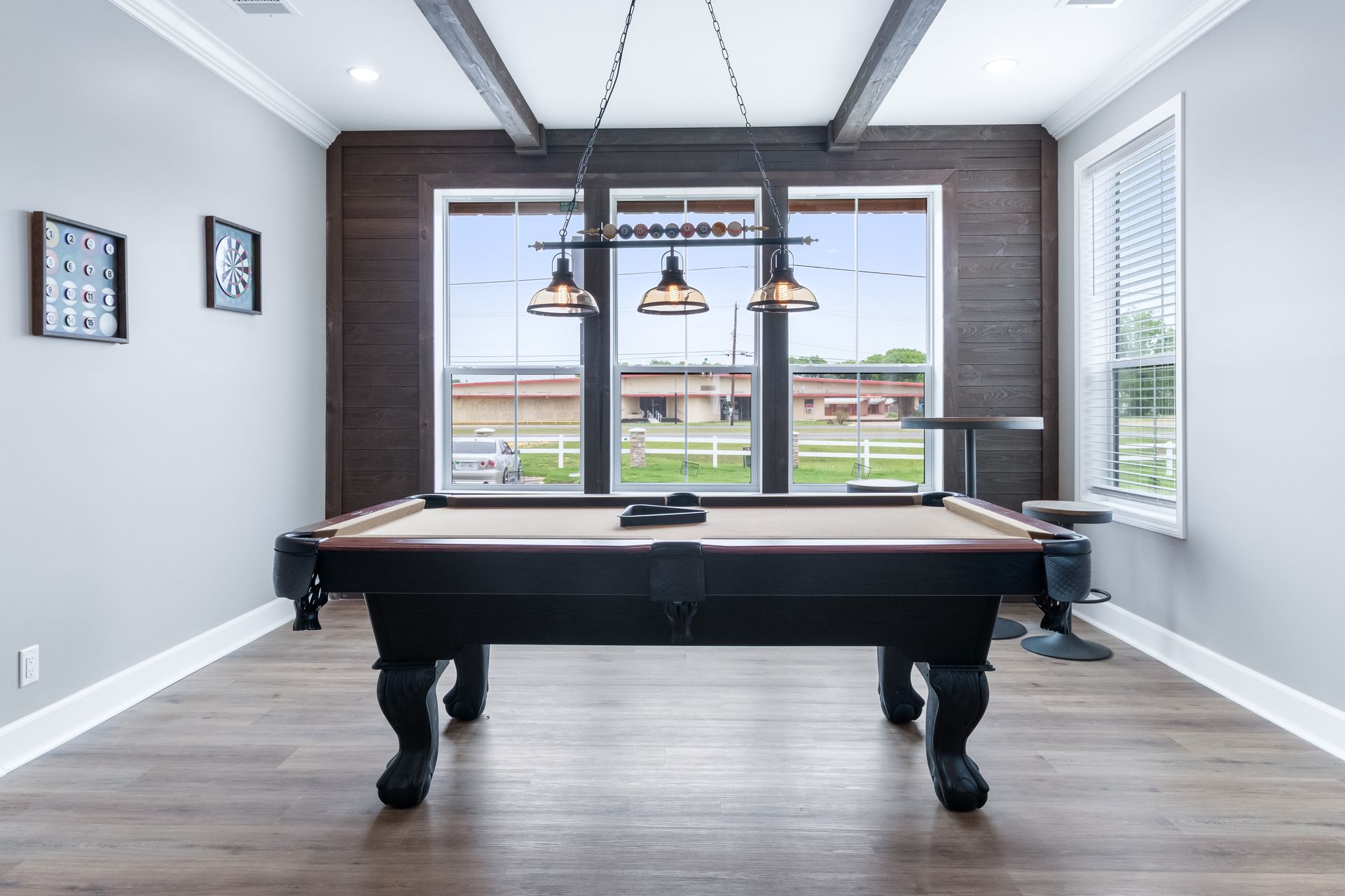 Modern game room with a black pool table, pendant lights, and large windows overlooking a field