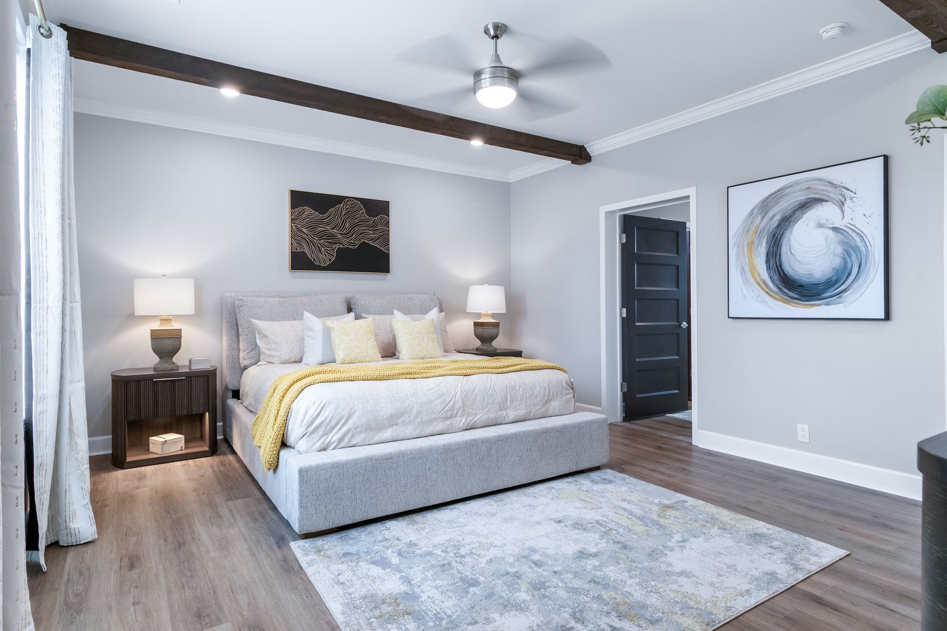 Bright modern bedroom with a gray bed, white walls, wood floor, and abstract wall art