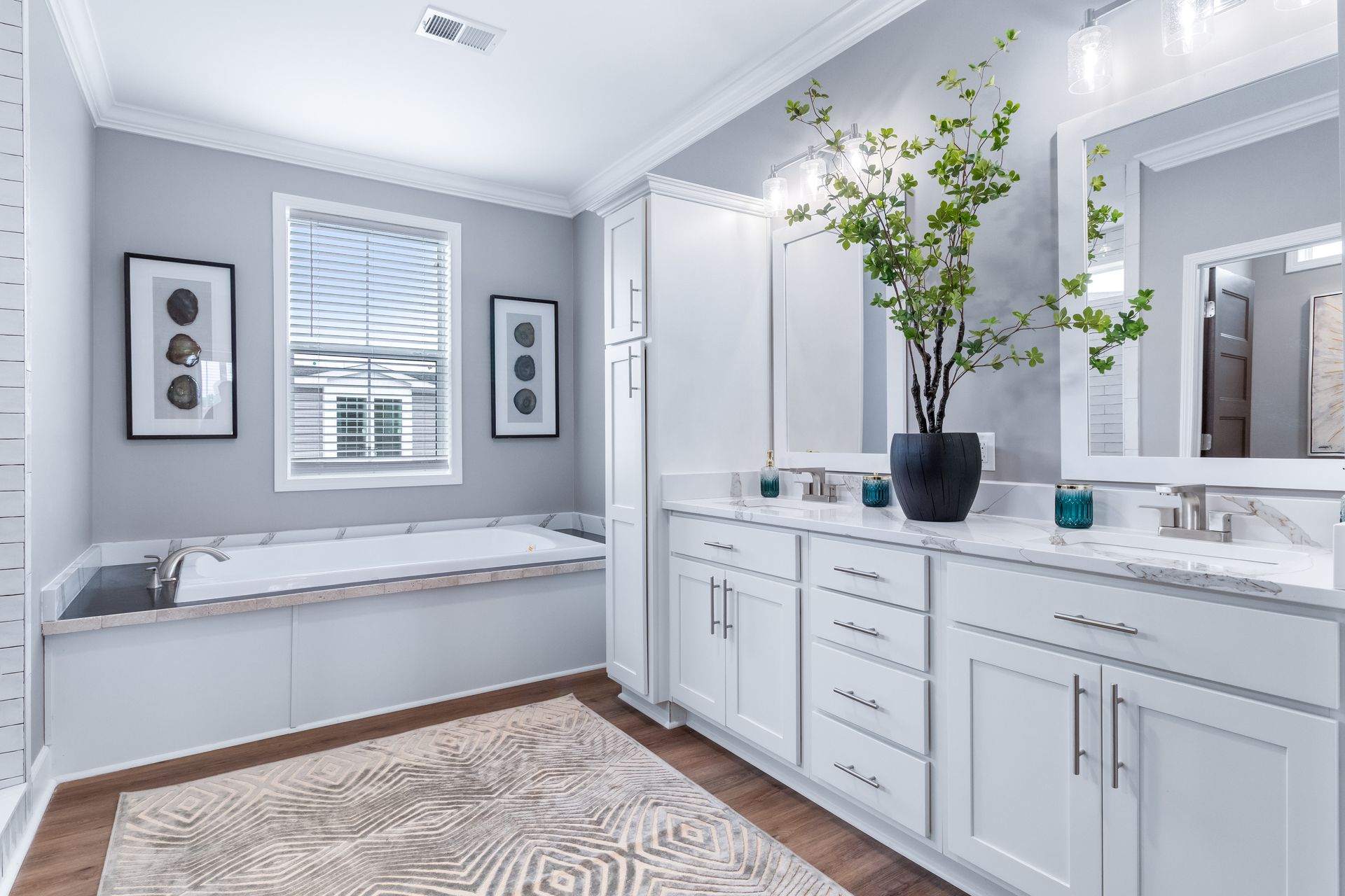 Bright white bathroom with a soaking tub, vanity, and large mirror, accented by a green plant and gray walls.