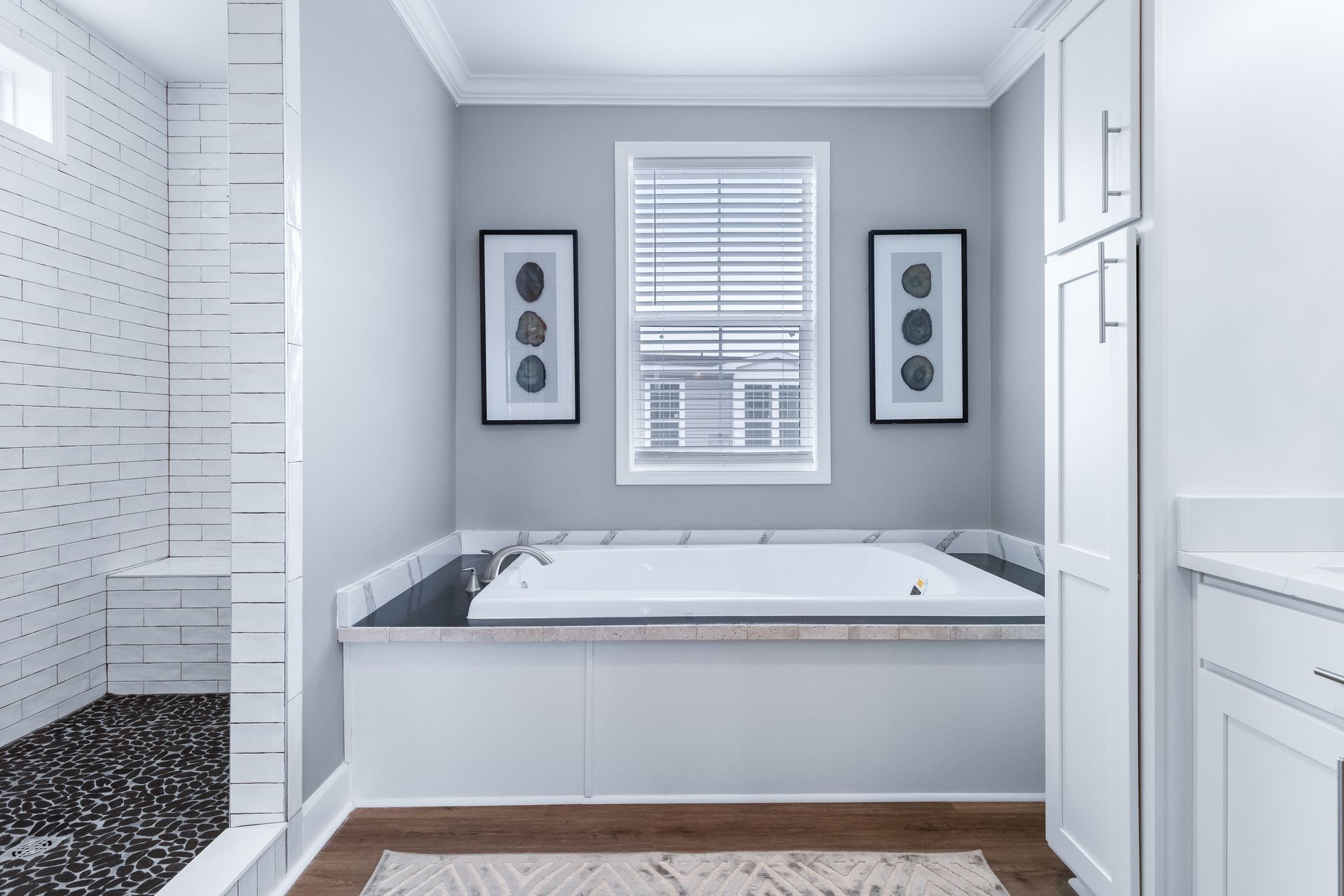 Bright white bathroom with a freestanding tub, window, framed wall art, and adjacent tiled shower.