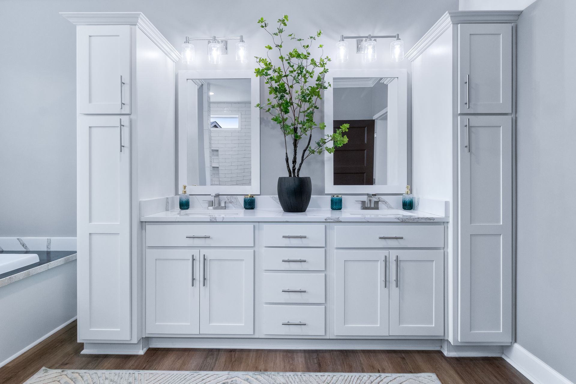 Modern white bathroom vanity with double mirrors, gray cabinets, and a black vase of green branches