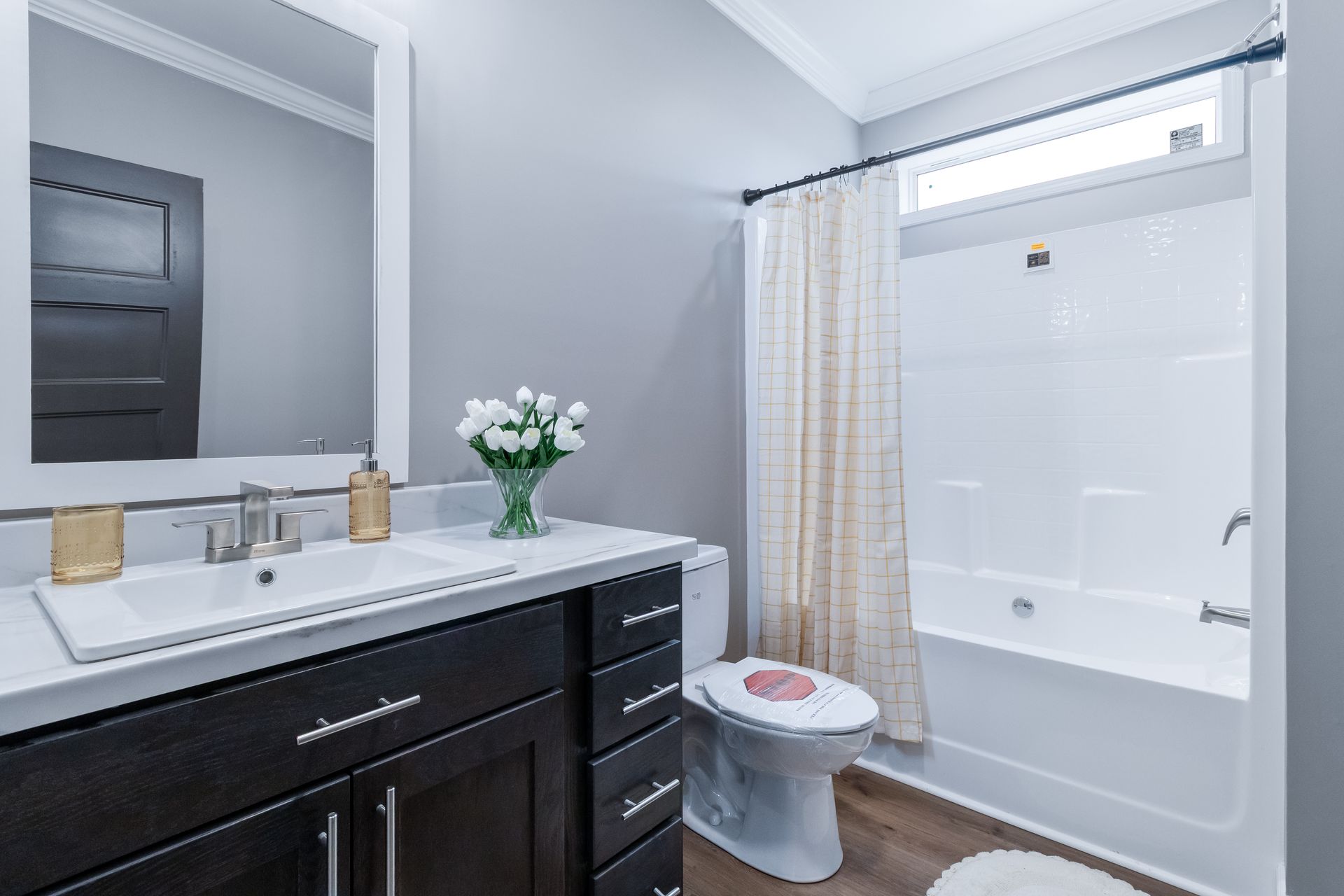 Modern bathroom with dark vanity, white sink, mirror, toilet, and bathtub with shower curtain
