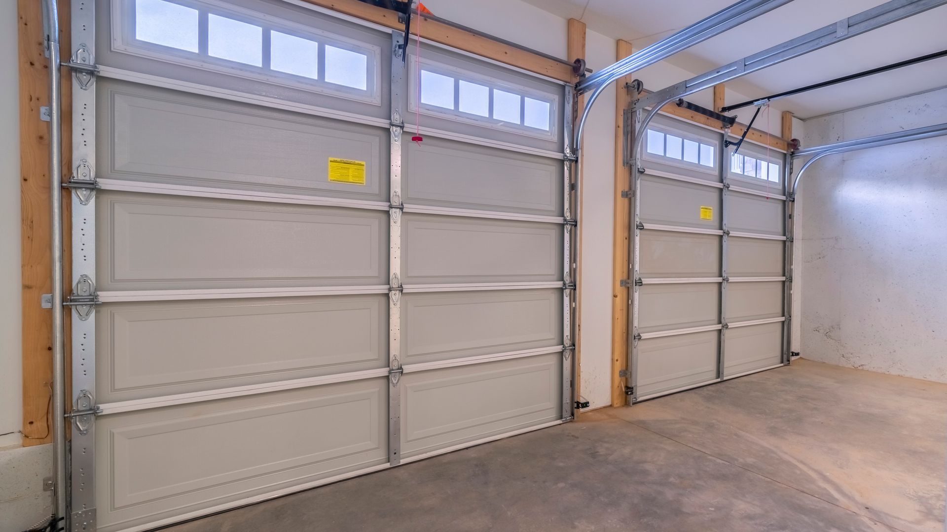 Empty garage with two white overhead doors and concrete floor